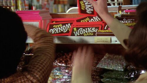 Hands reaching for Wonka chocolate bars on a shop shelf.