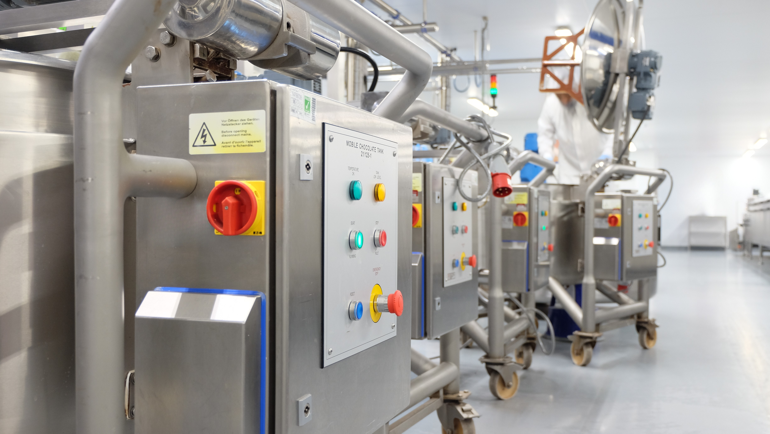 Four mobile chocolate tanks on wheels in a production environment. 