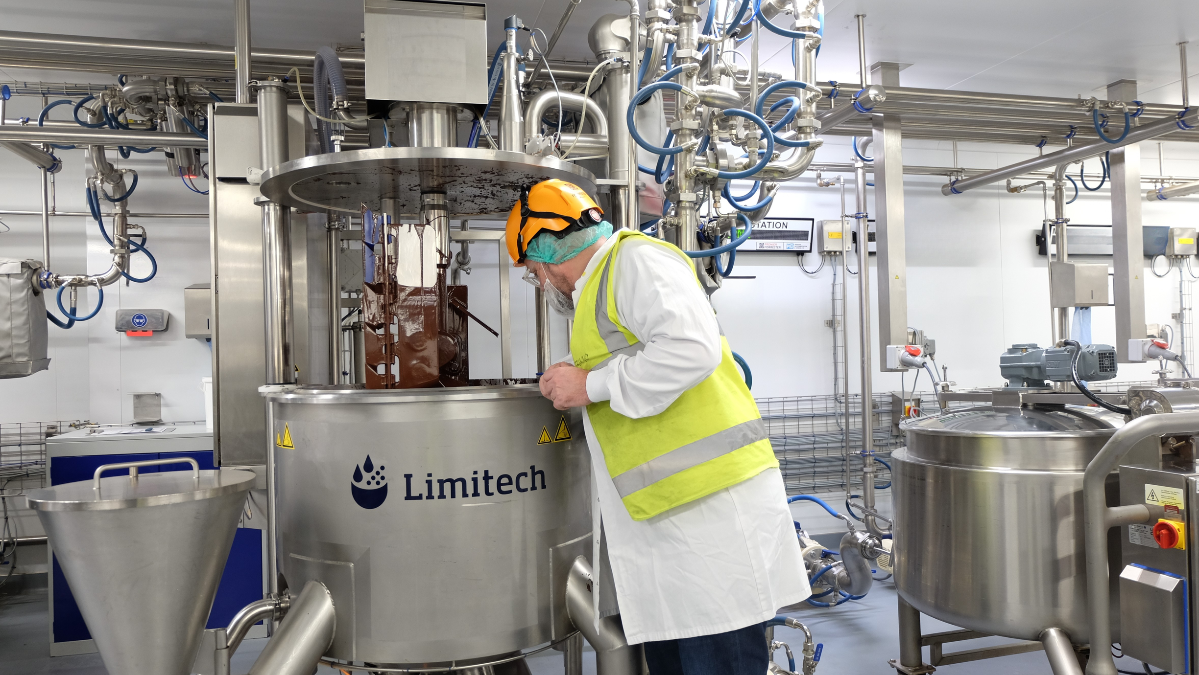 Factory worker in protective clothing inspecting milk chocolate inside a chocolate tank.