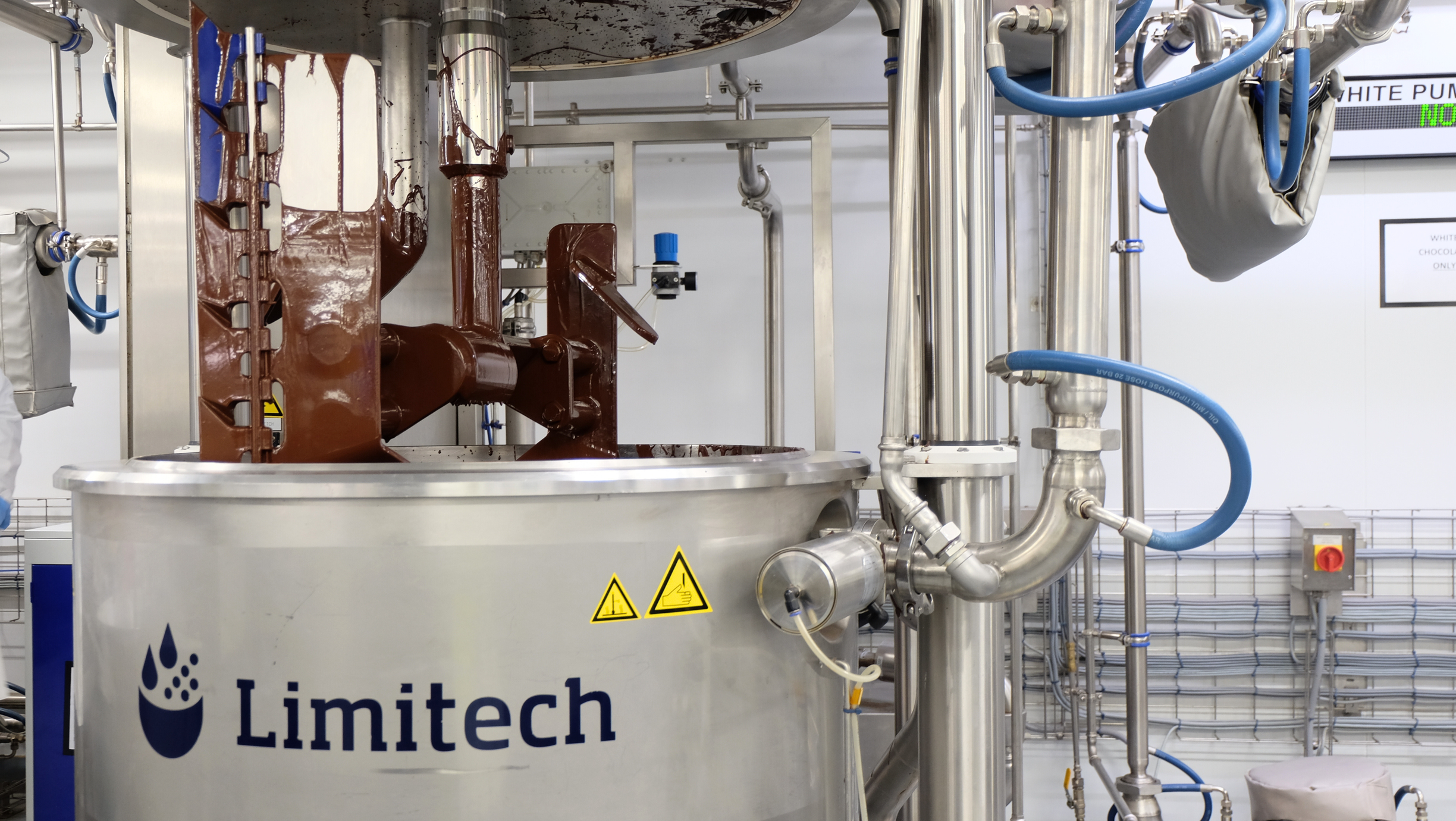 Limitech-branded chocolate machine with connected pipes in an industrial facility.