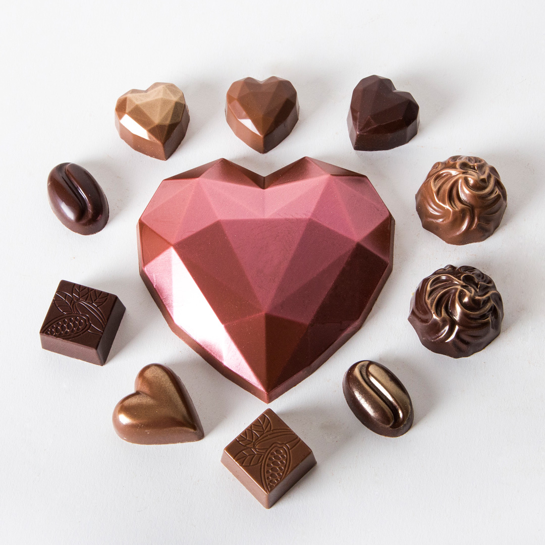 Assorted moulded chocolates arranged around a large chocolate heart on a white background.