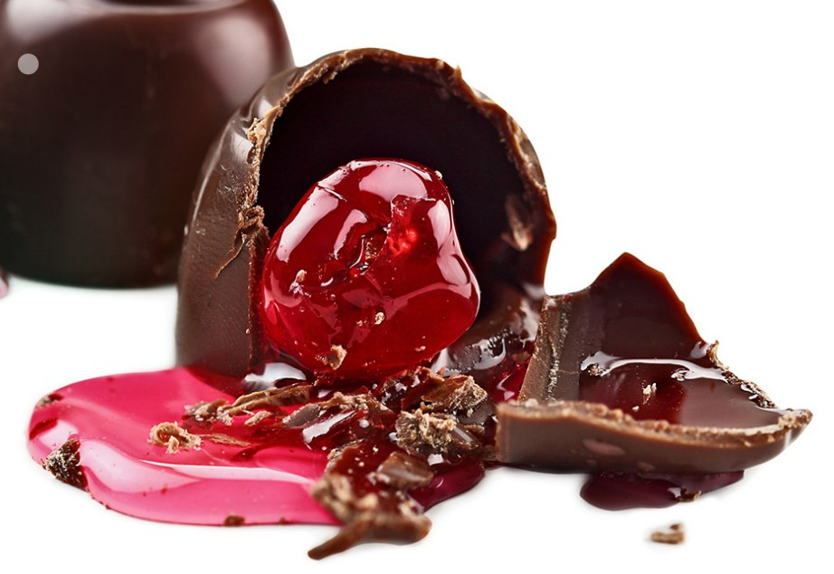 Two milk chocolate shells on a white surface. One is broken showing a runny red cherry centre.
