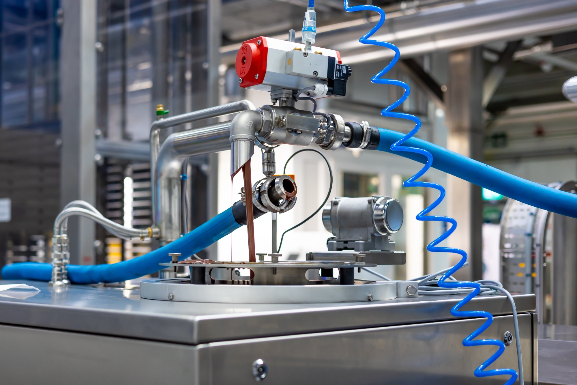 Milk chocolate drips from a nozzle in an industrial chocolate production facility.