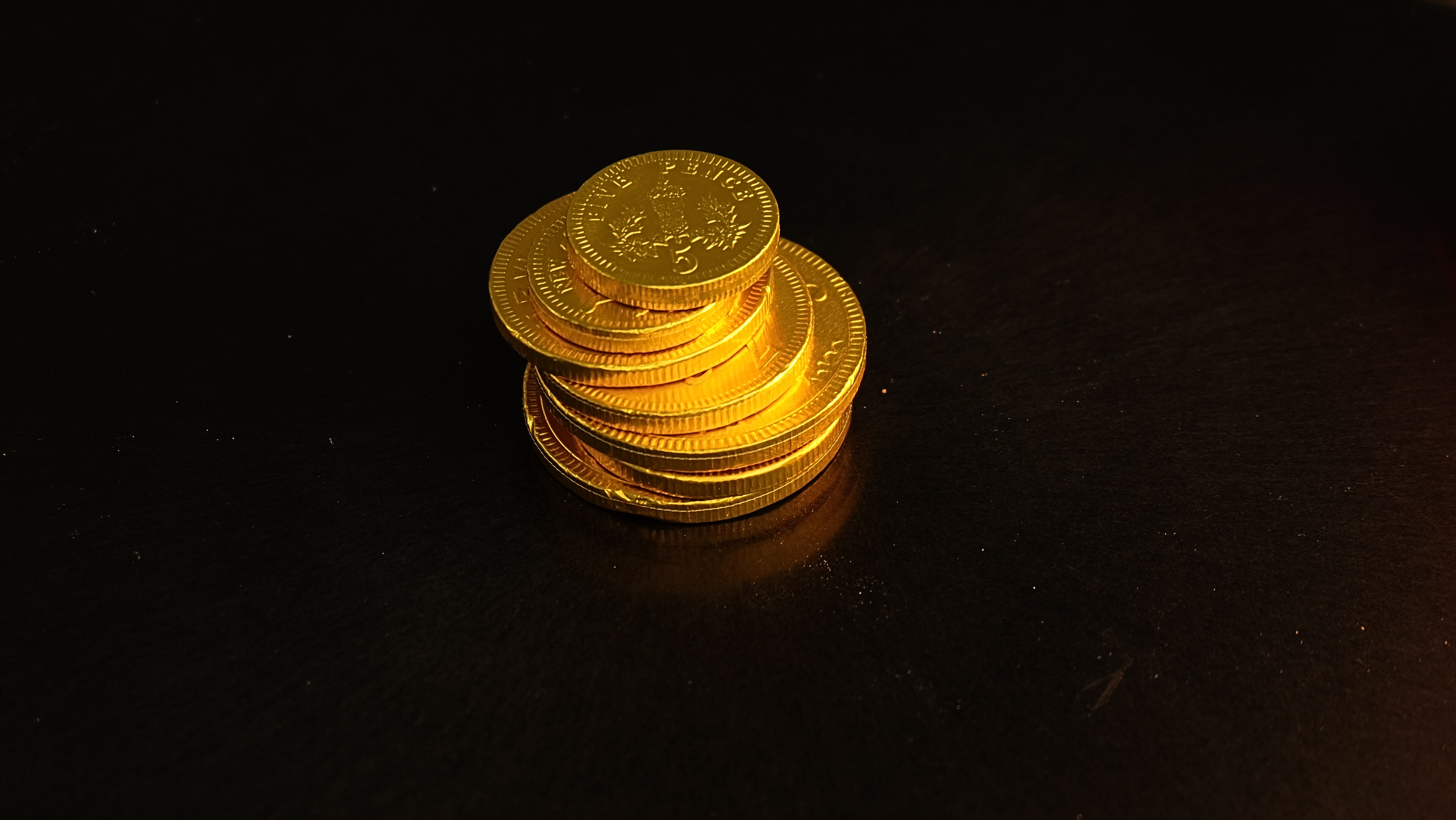 An assortment of novelty festive chocolate coins wrapped in gold foil on a dark surface.