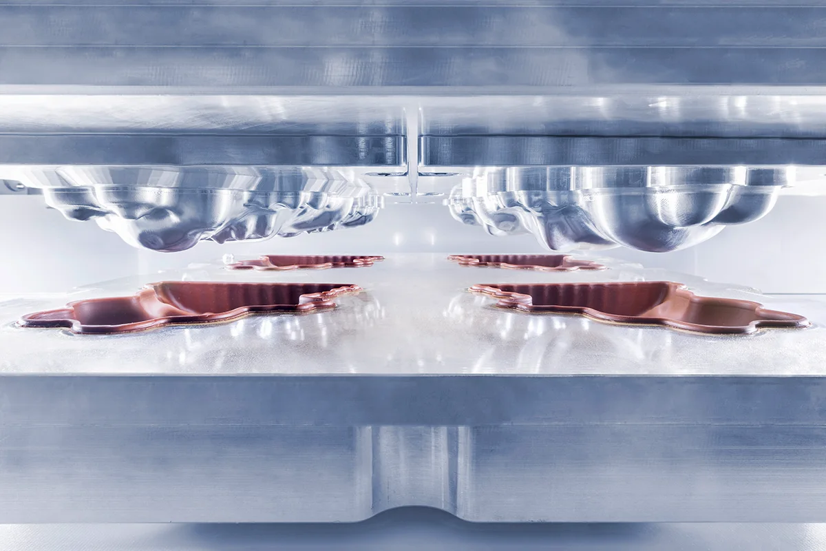 Close-up of a cold press machine forming liquid chocolate into metal moulds.