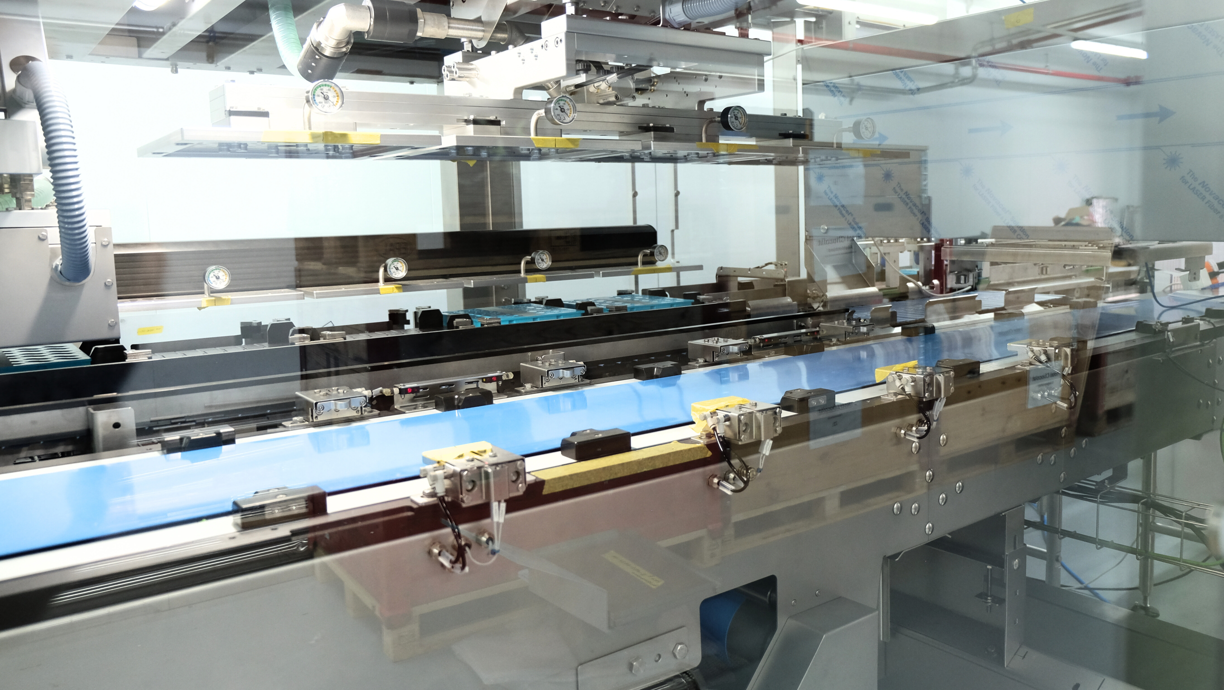 Industrial demoulding machine with conveyor and pressure gauges behind a glass safety cover.