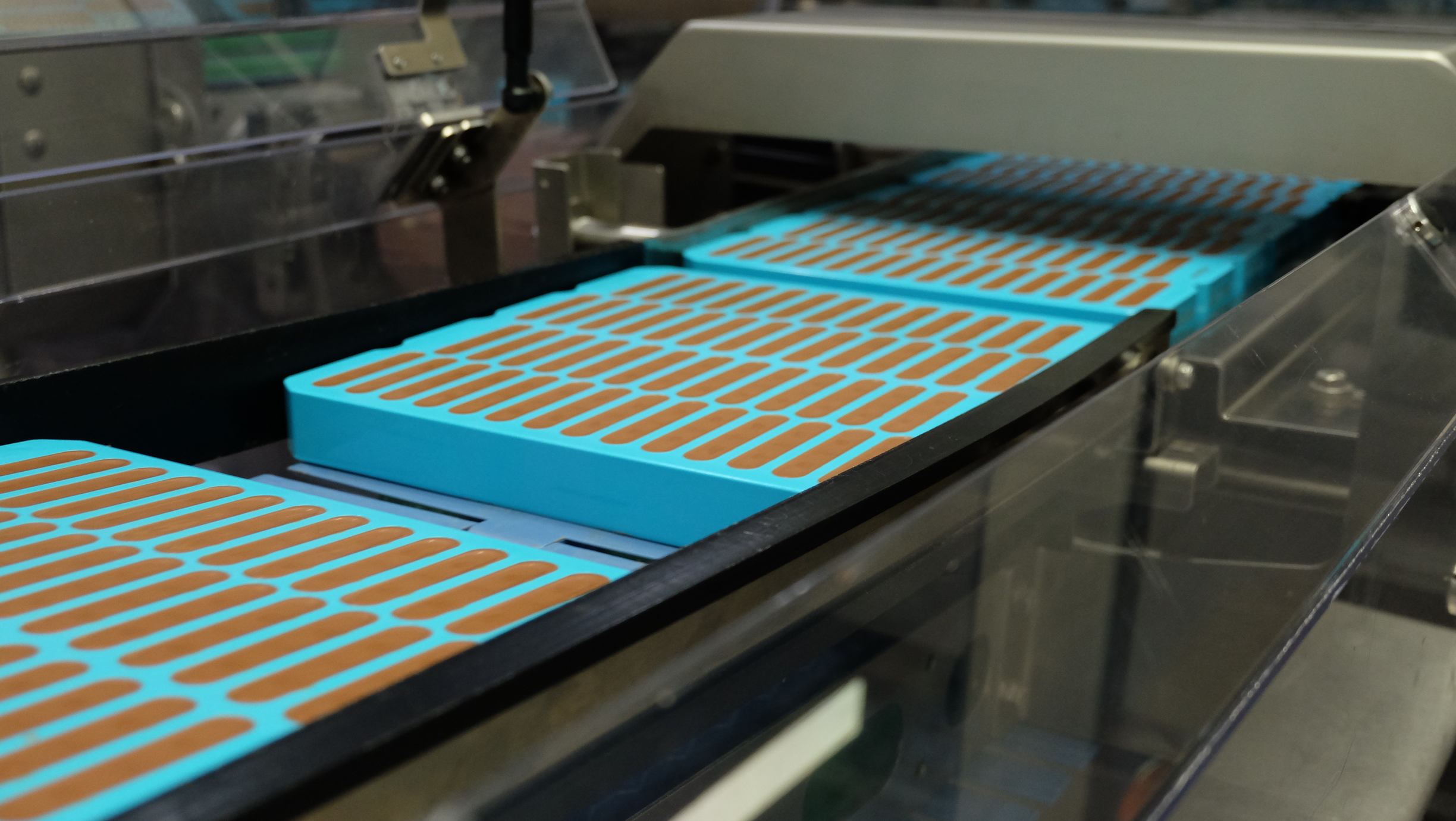 Blue silicone moulds with chocolate bars on automated conveyor during industrial demoulding.