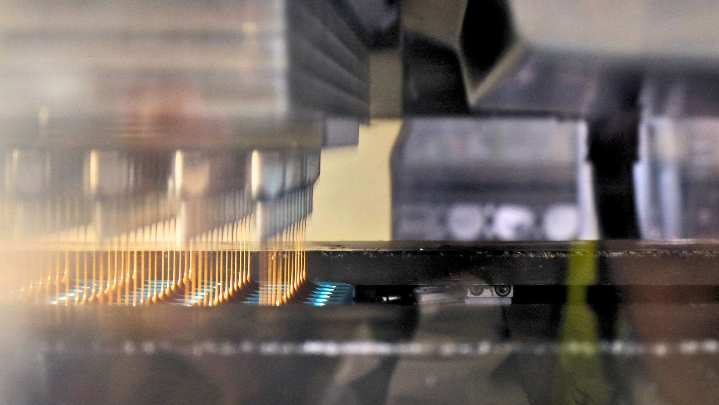 Close-up of industrial depositing machine dispensing liquid chocolate through multiple nozzles.