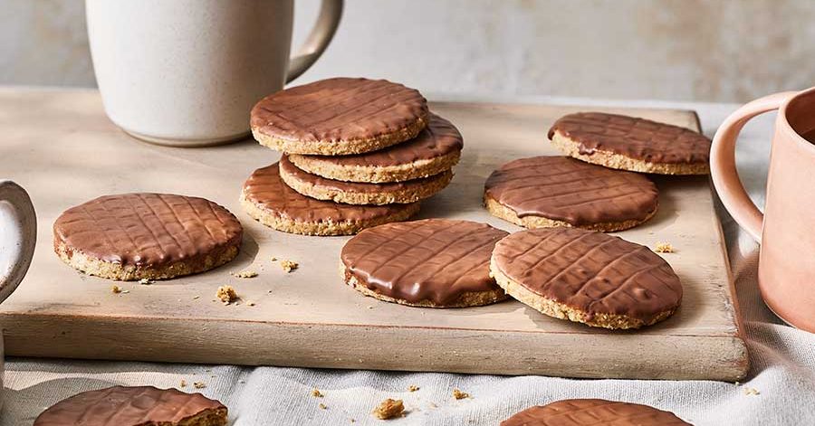 Milk chocolate coated digestive biscuits scattered on a wooden surface.