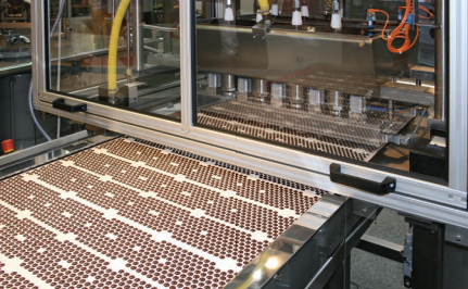 An industrial drop depositor machine dispensing milk chocolate drops in rows.