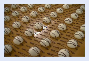 Rows of round white chocolates with dark drizzle decoration on conveyor belt.