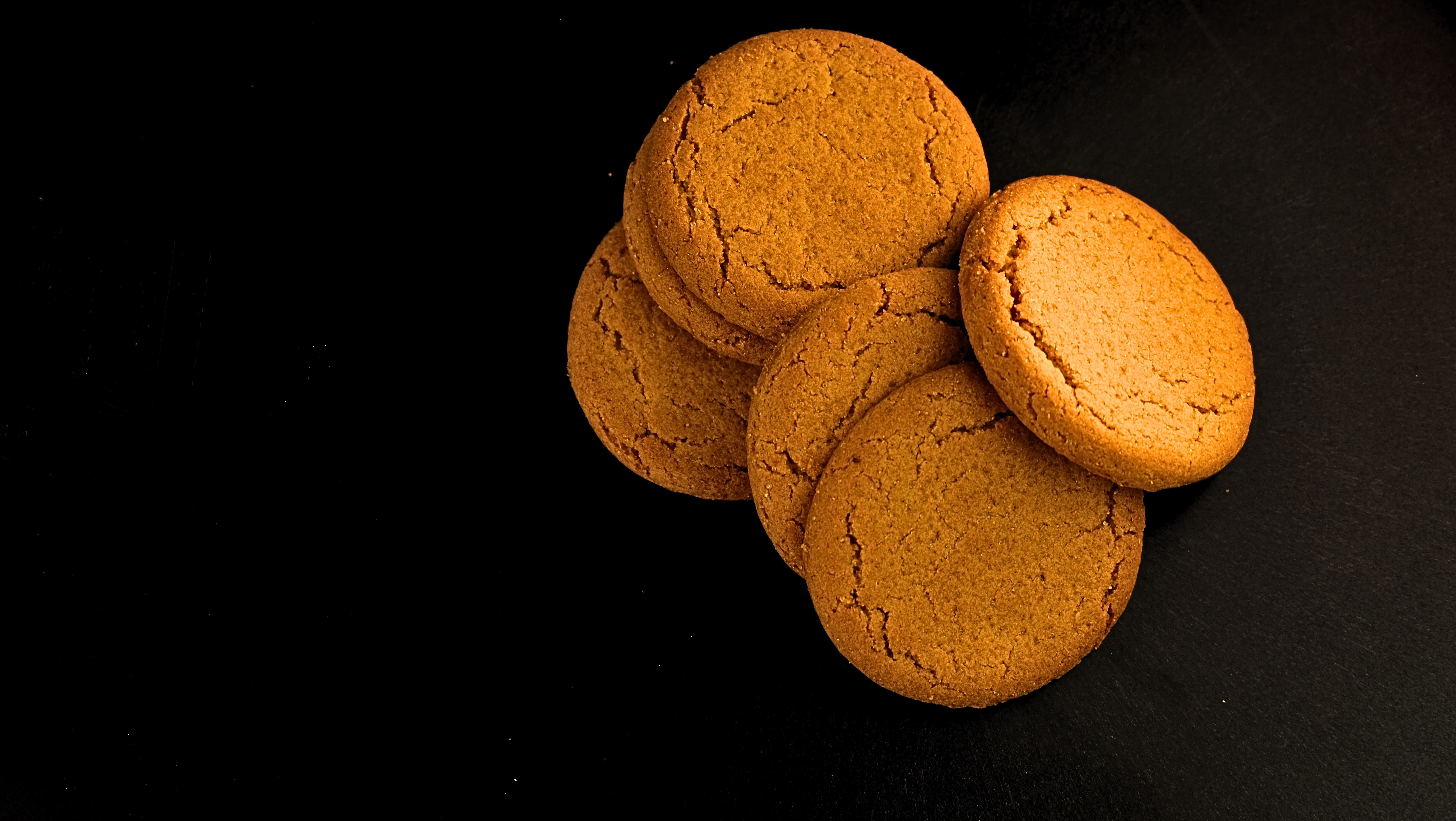 Looking down on six ginger biscuits placed on a dark surface.