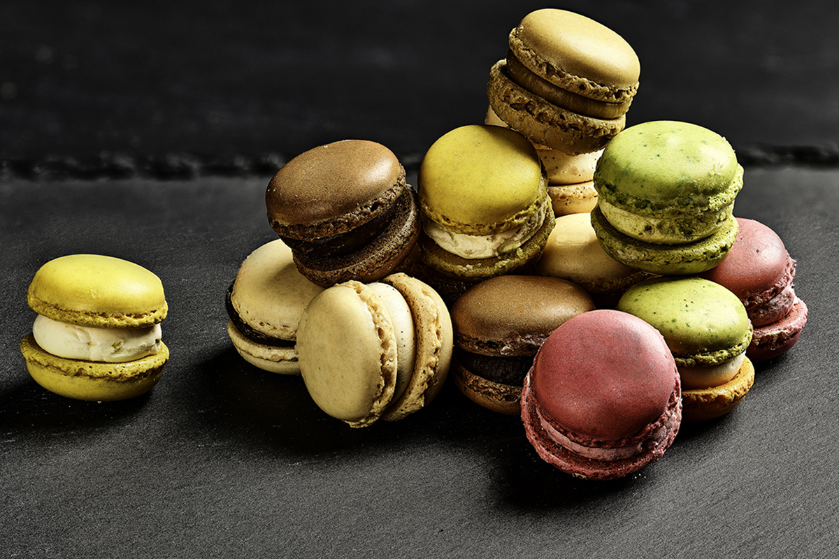 A pile of colourful macarons in assorted flavours, including green, yellow, brown, and red.
