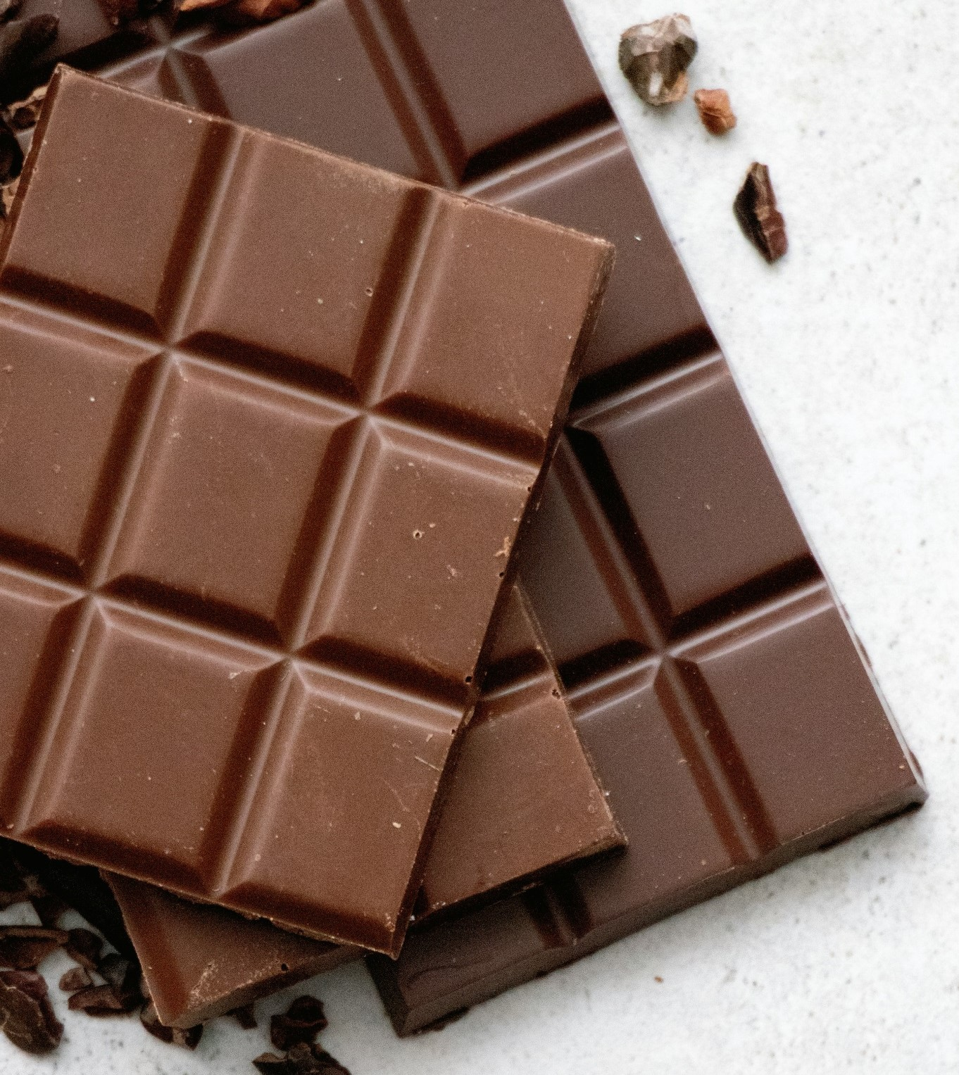 A close-up of three solid milk chocolate bars stacked on top of each other on a light surface.