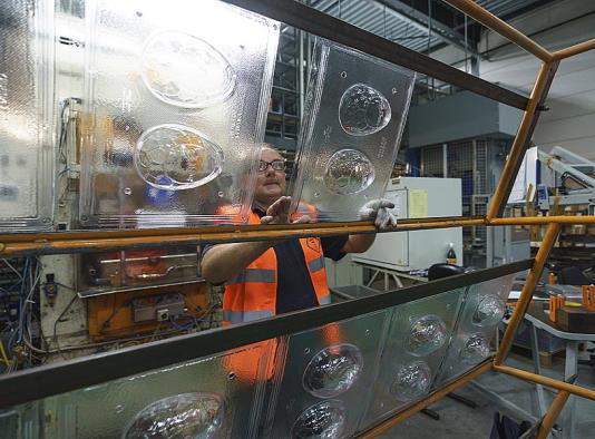 A factory worker handling large plastic thermoform Easter egg chocolate moulds on a metal rack.