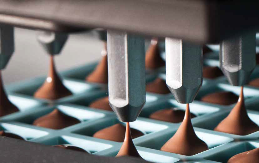 A Trikno chocolate depositor filling individual square chocolate moulds with liquid chocolate.