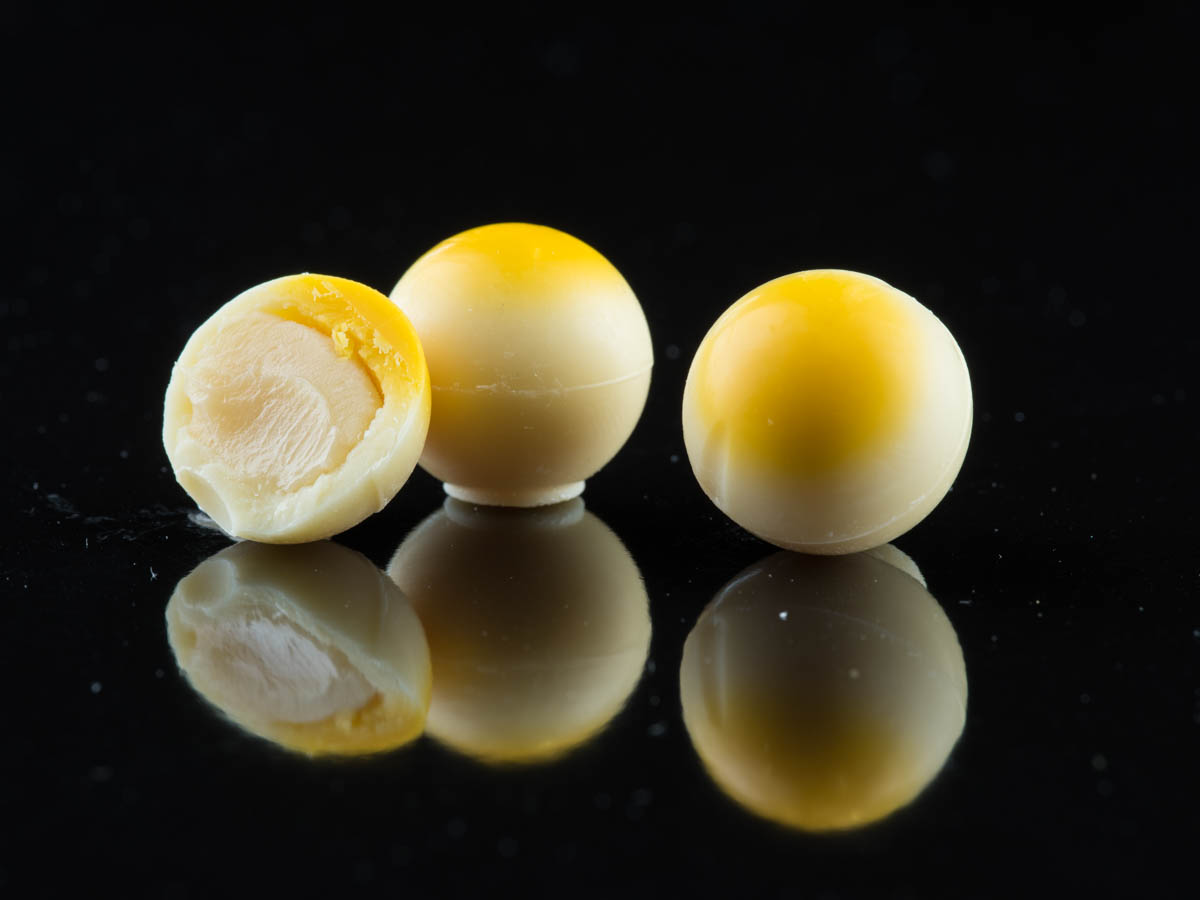 Three white chocolate balls topped with a yellow dot, placed on a reflective back surface.
