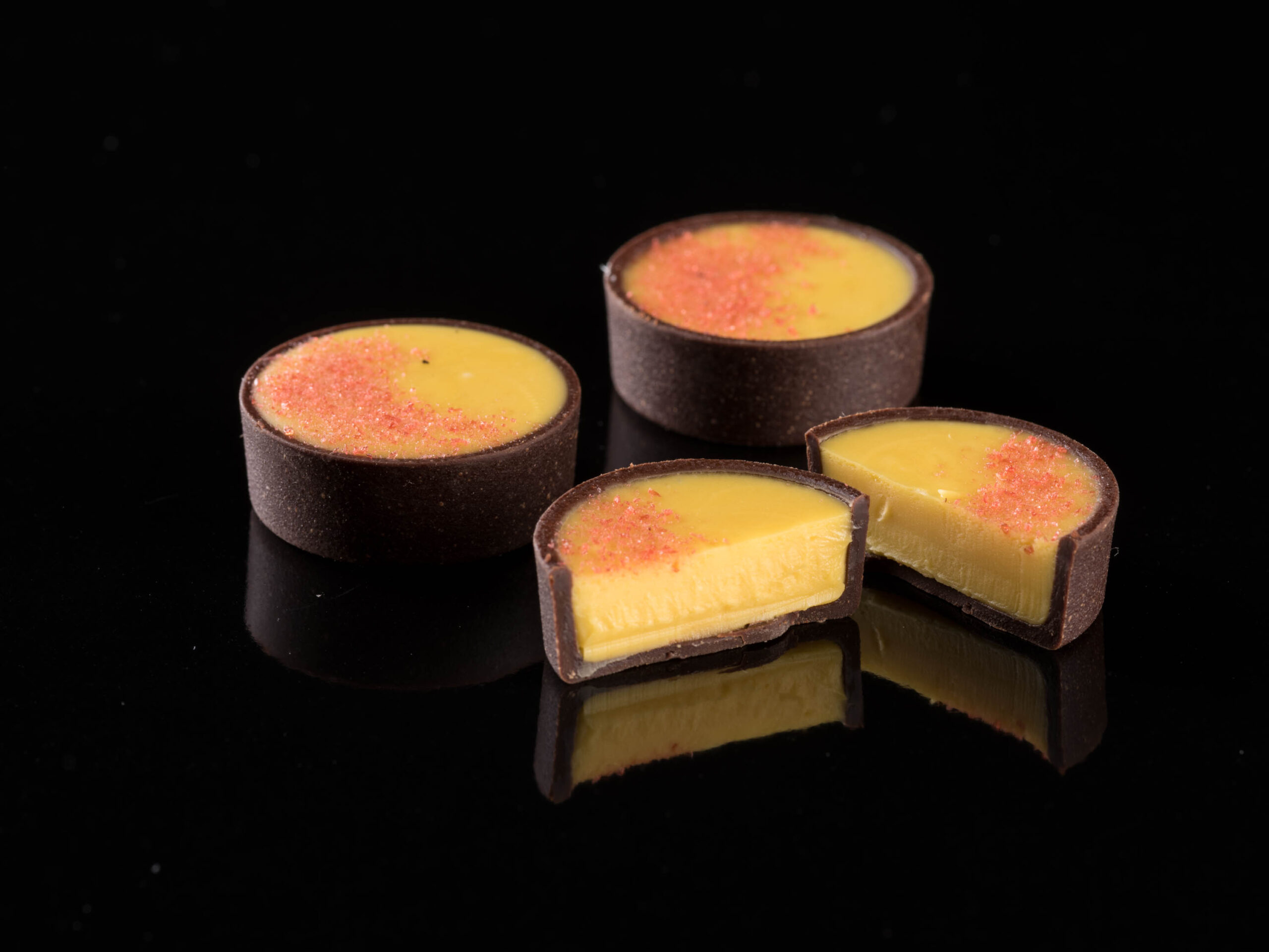 Three milk chocolate cups with a yellow filling, partially topped with red sprinkles.