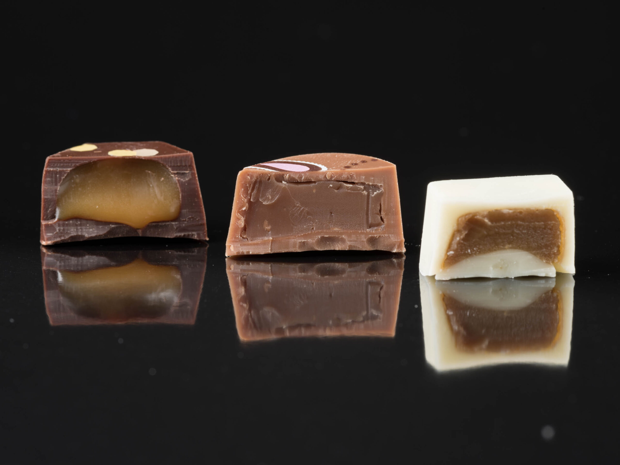 Three assorted filled chocolates cut in half to show caramel and truffle centres.