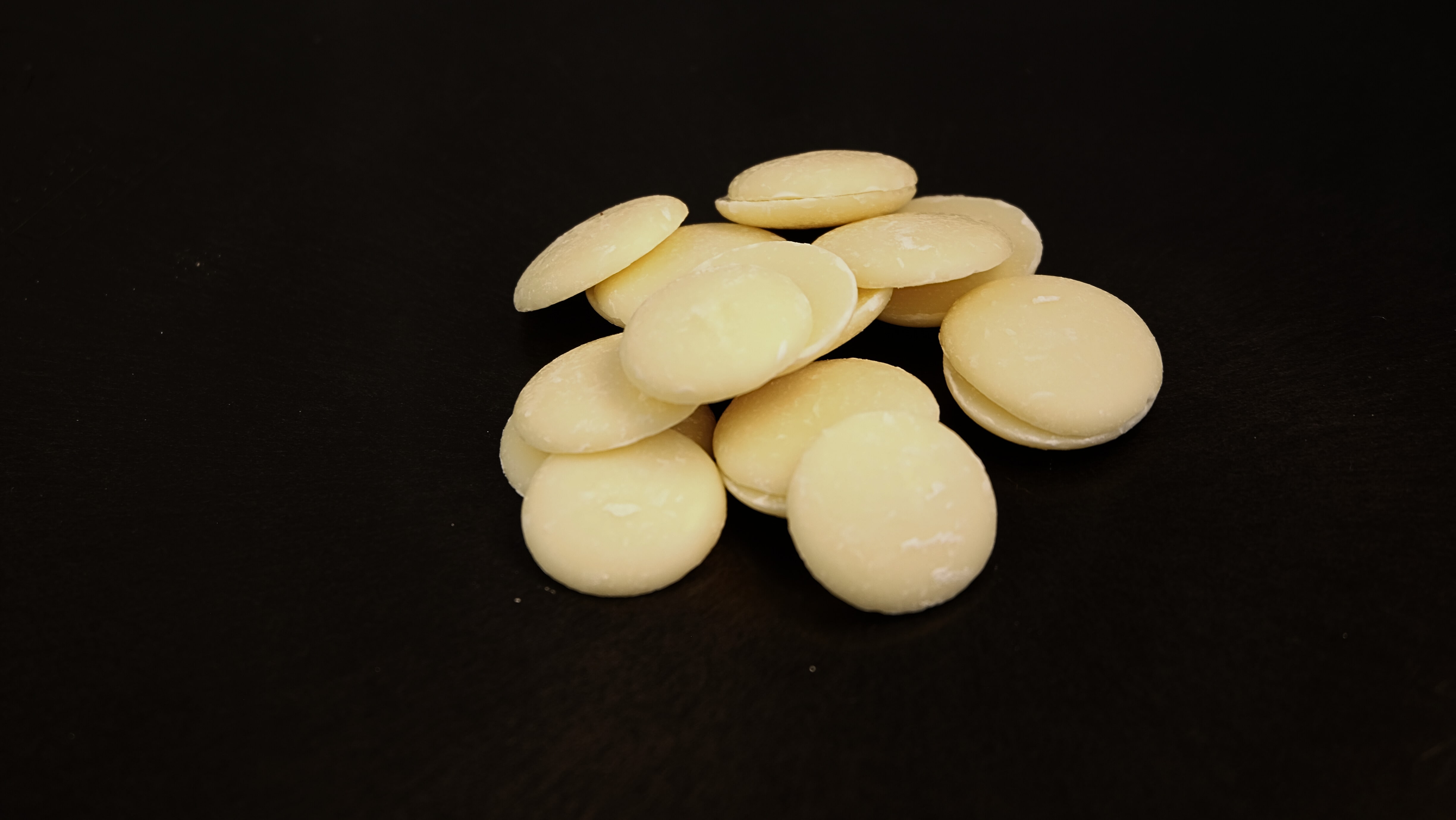 A handful of white chocolate buttons scattered on a black surface.