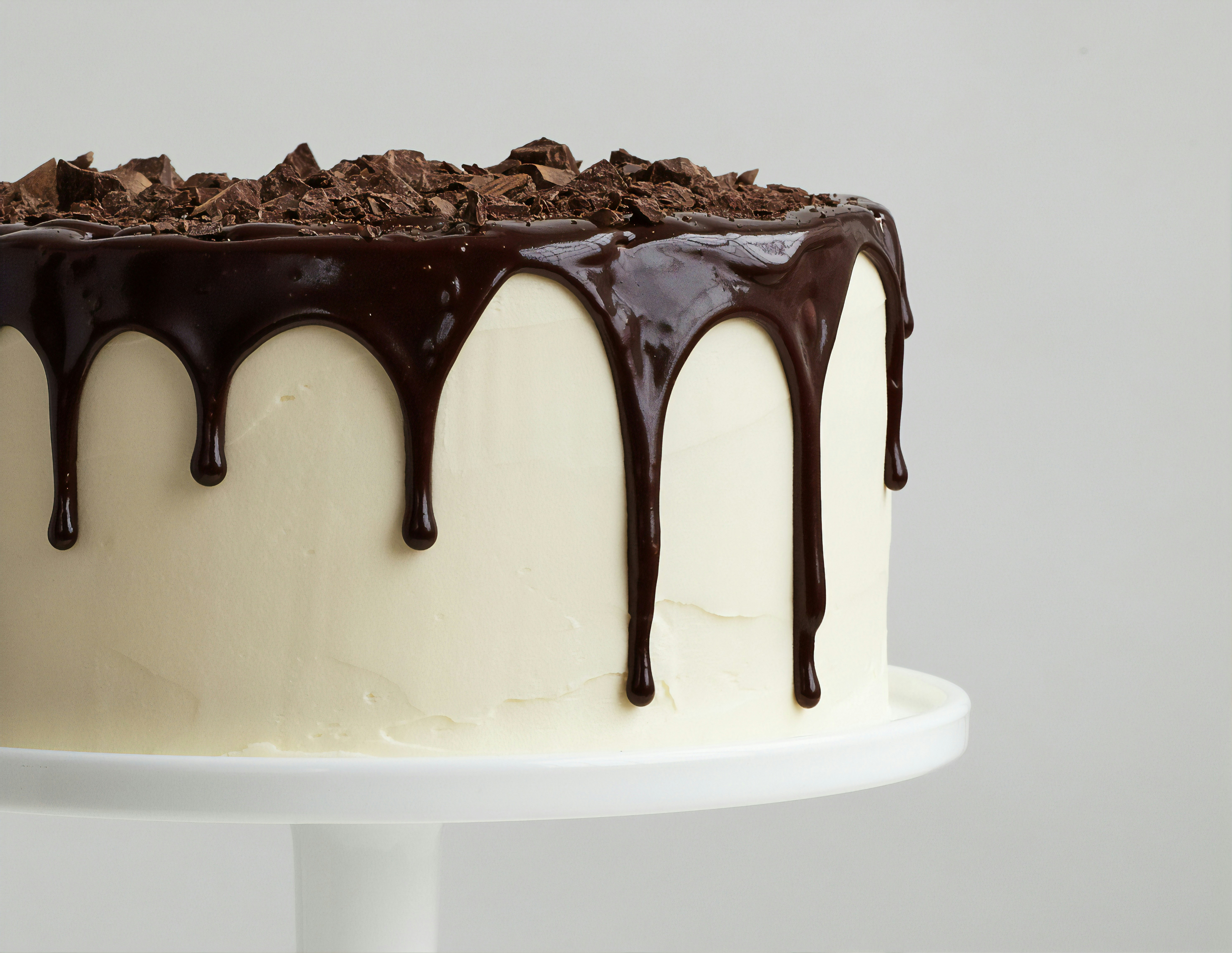 Chocolate cake with smooth white icing topped with chocolate ganache drips and chocolate pieces.