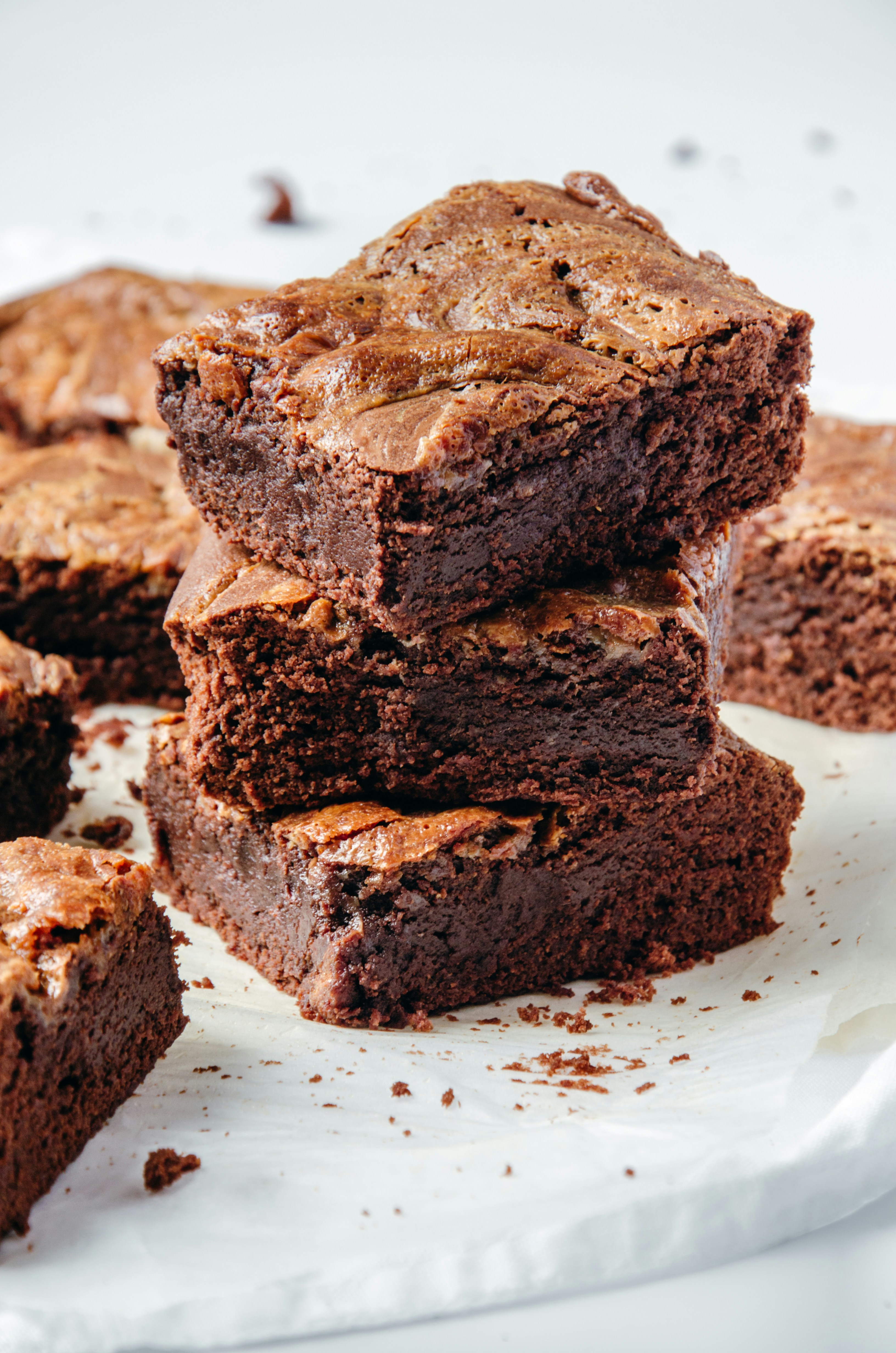 A stack of three freshly baked chocolate brownies surrounded by other brownie pieces.