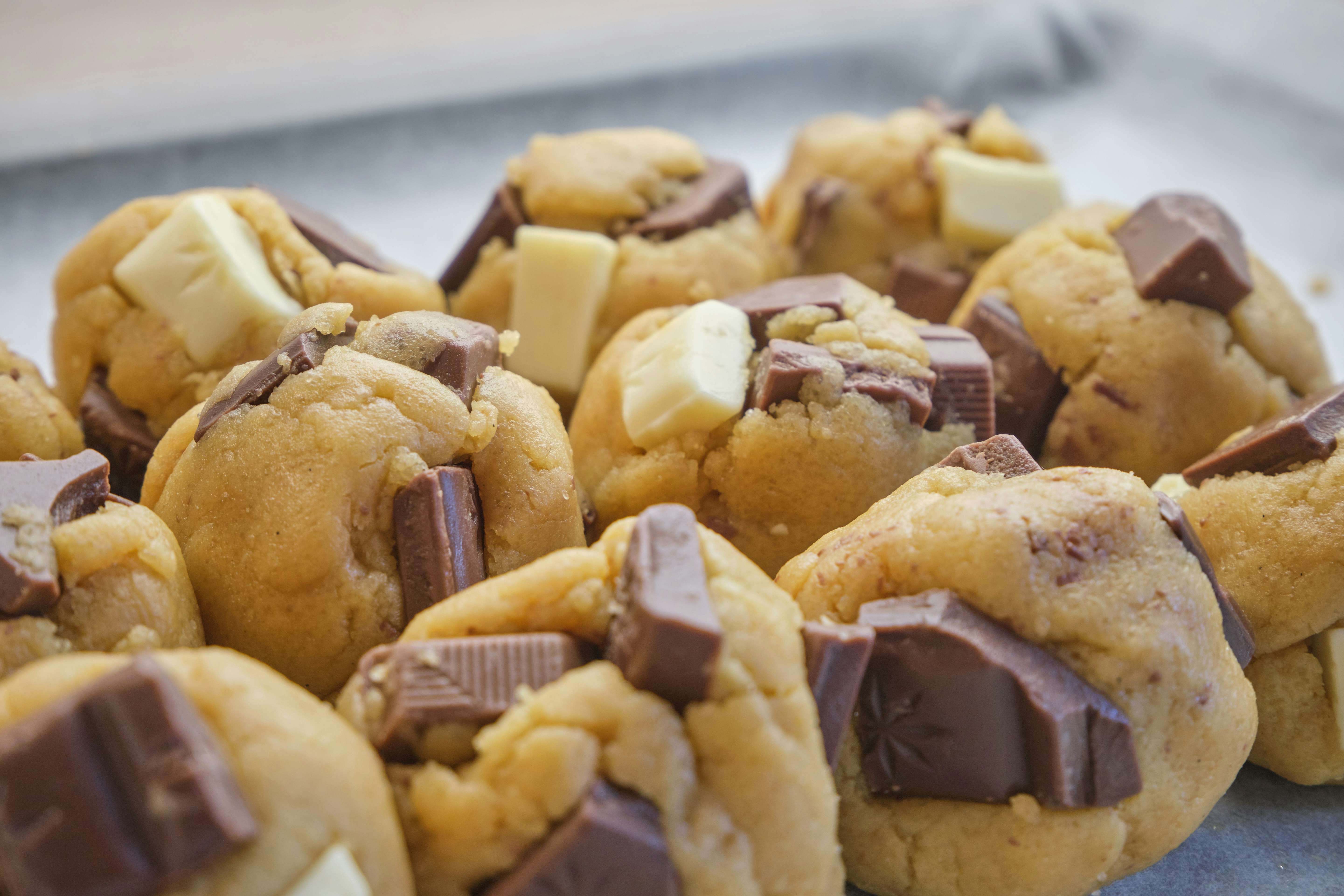 Balls of cookie dough mixed with chunks of milk and white chocolate on a baking tray.