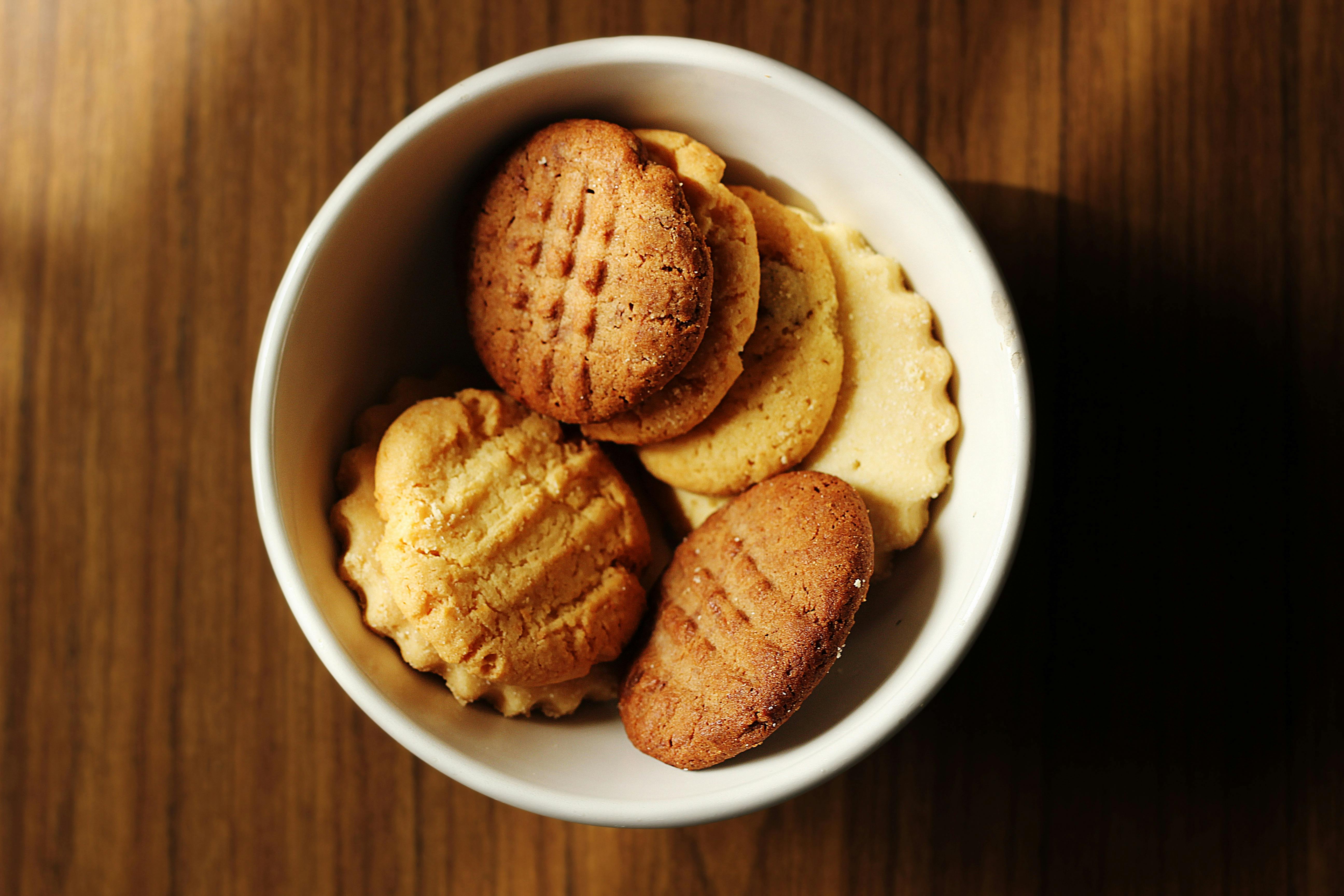A small white bowl holding an assortment of biscuits on a wooden surface.