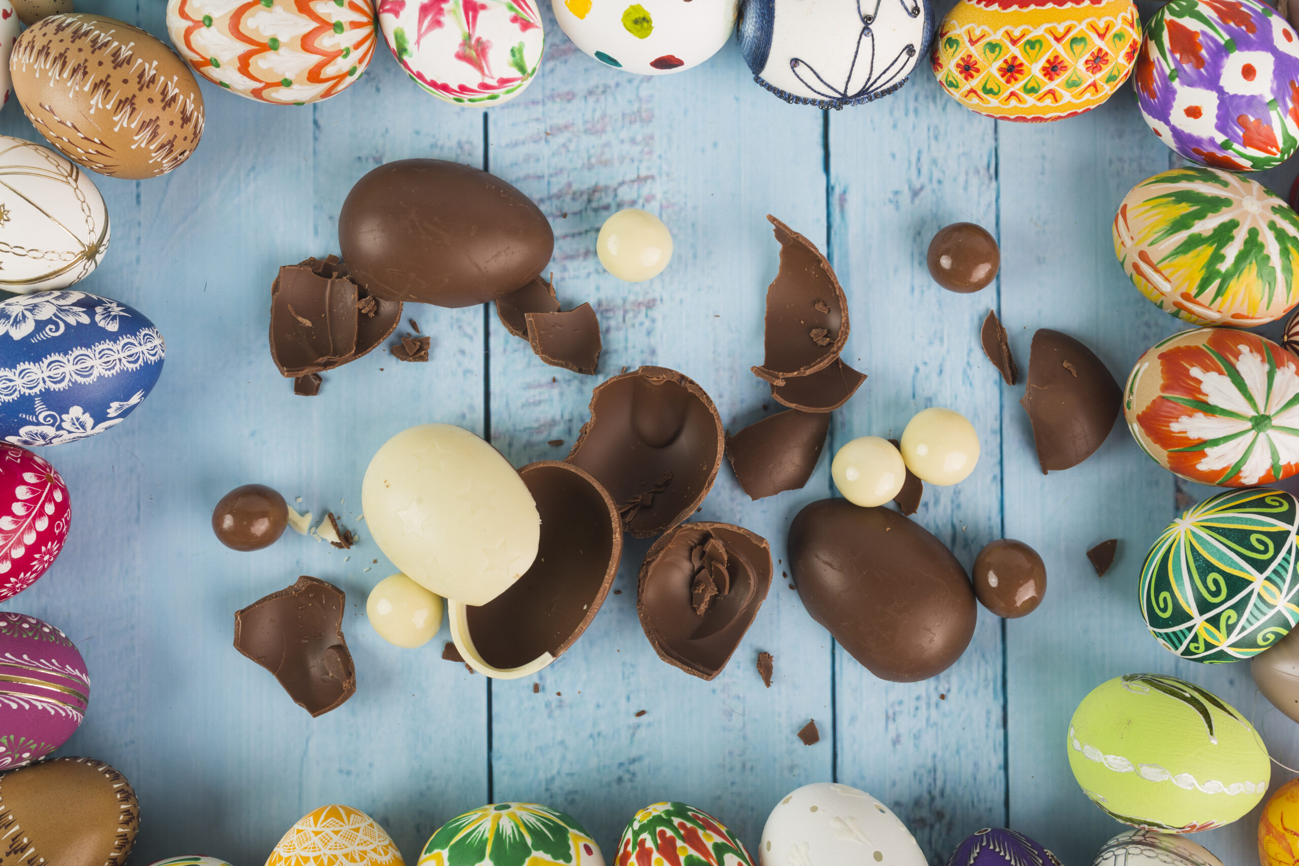An assortment of milk and white chocolate easter eggs on a blue surface. 