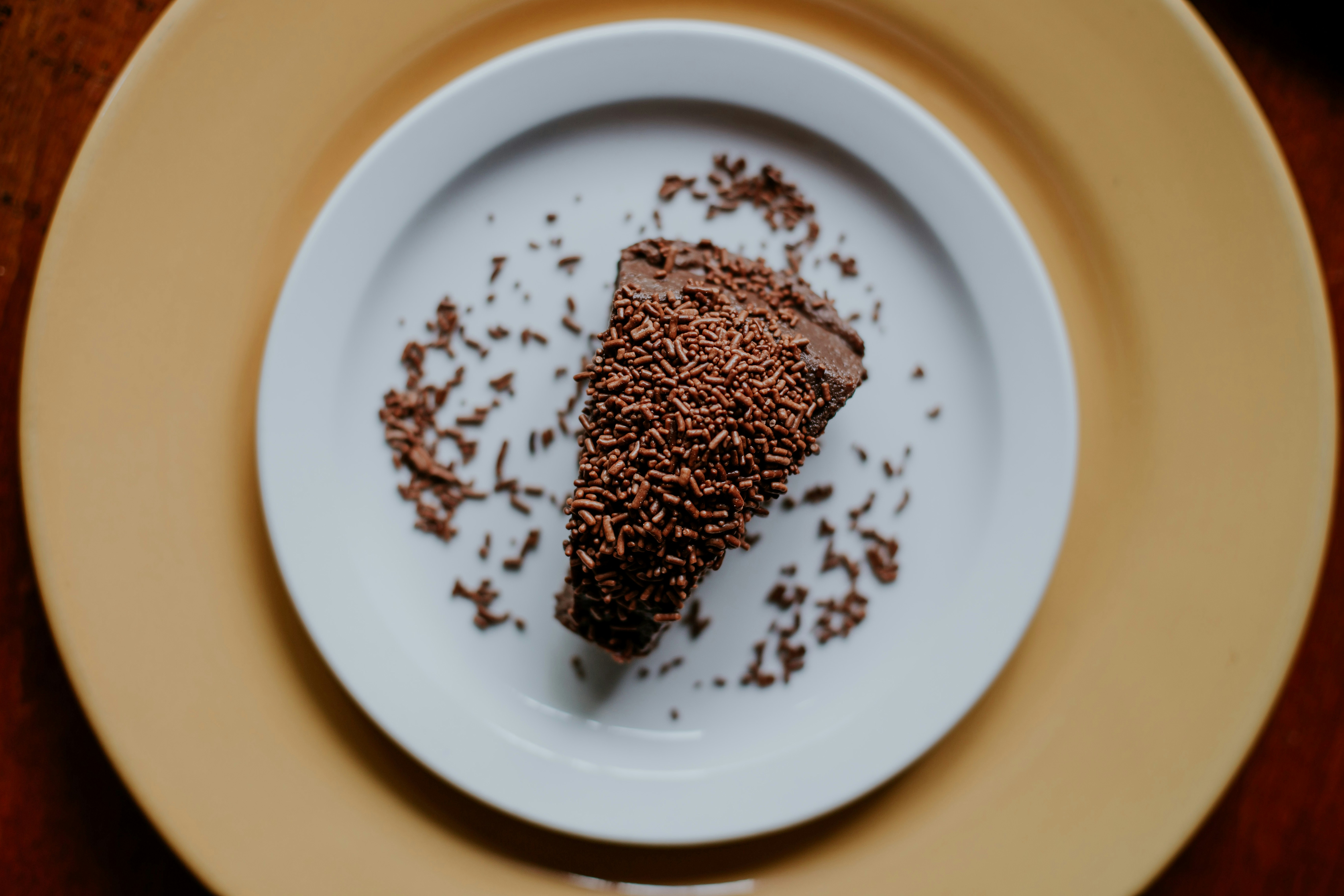Triangular piece of chocolate cake covered in milk chocolate sprinkles on a white plate.