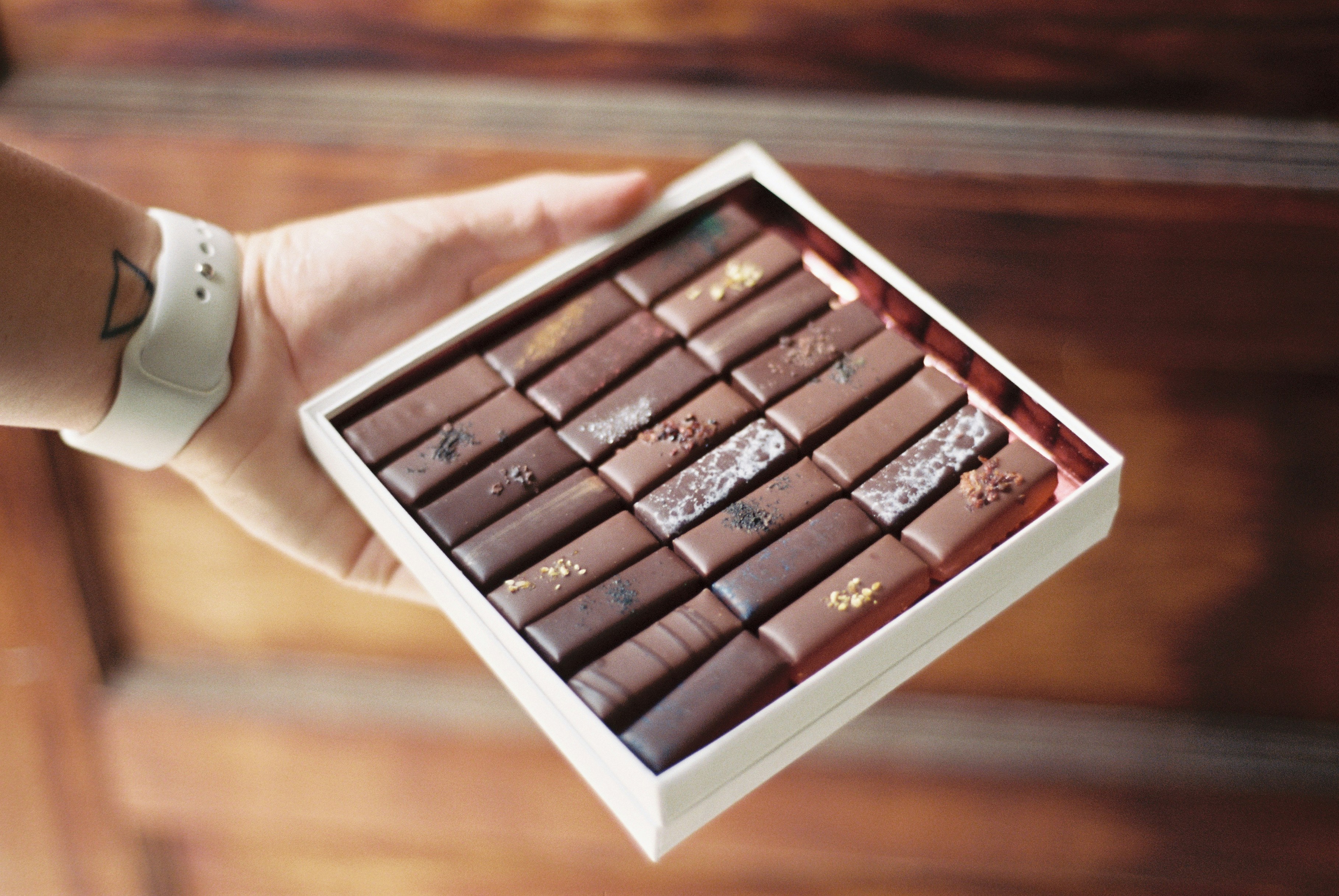 Hand holding a box of assorted chocolate bars, decorated with various toppings.