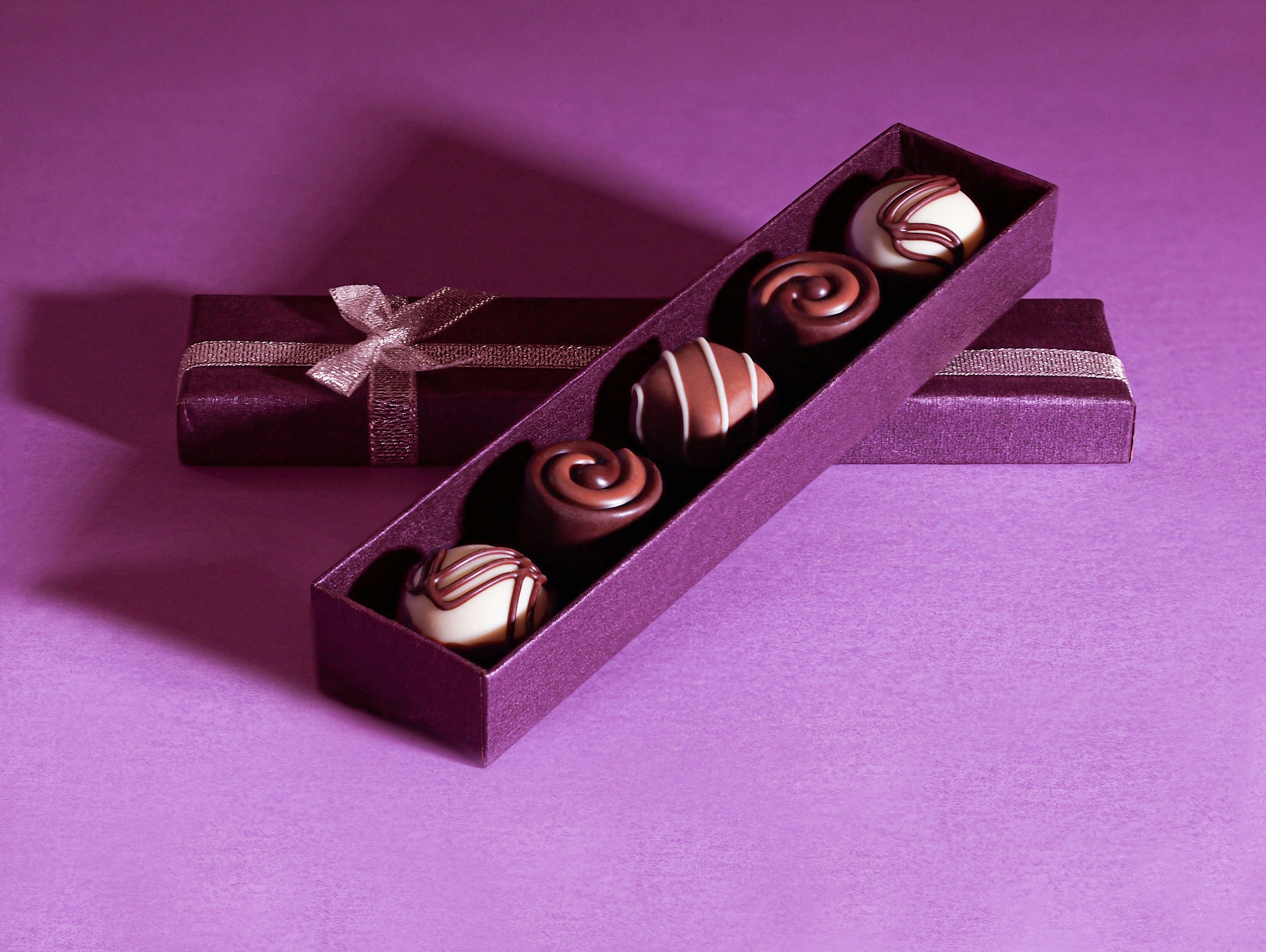Five assorted chocolates in a purple gift-wrapped box on a purple surface.