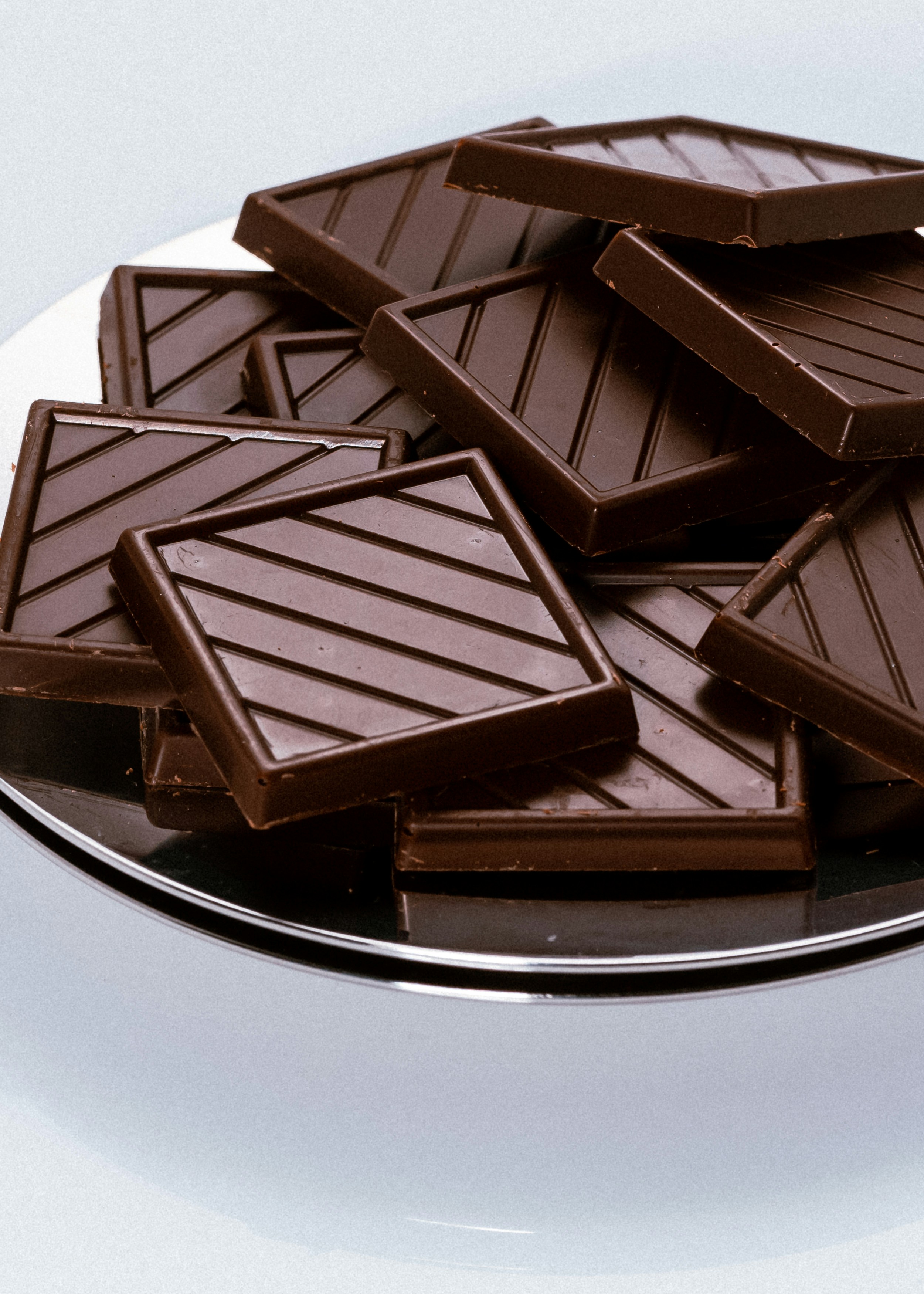 Silver plate of dark chocolate squares on a white surface.