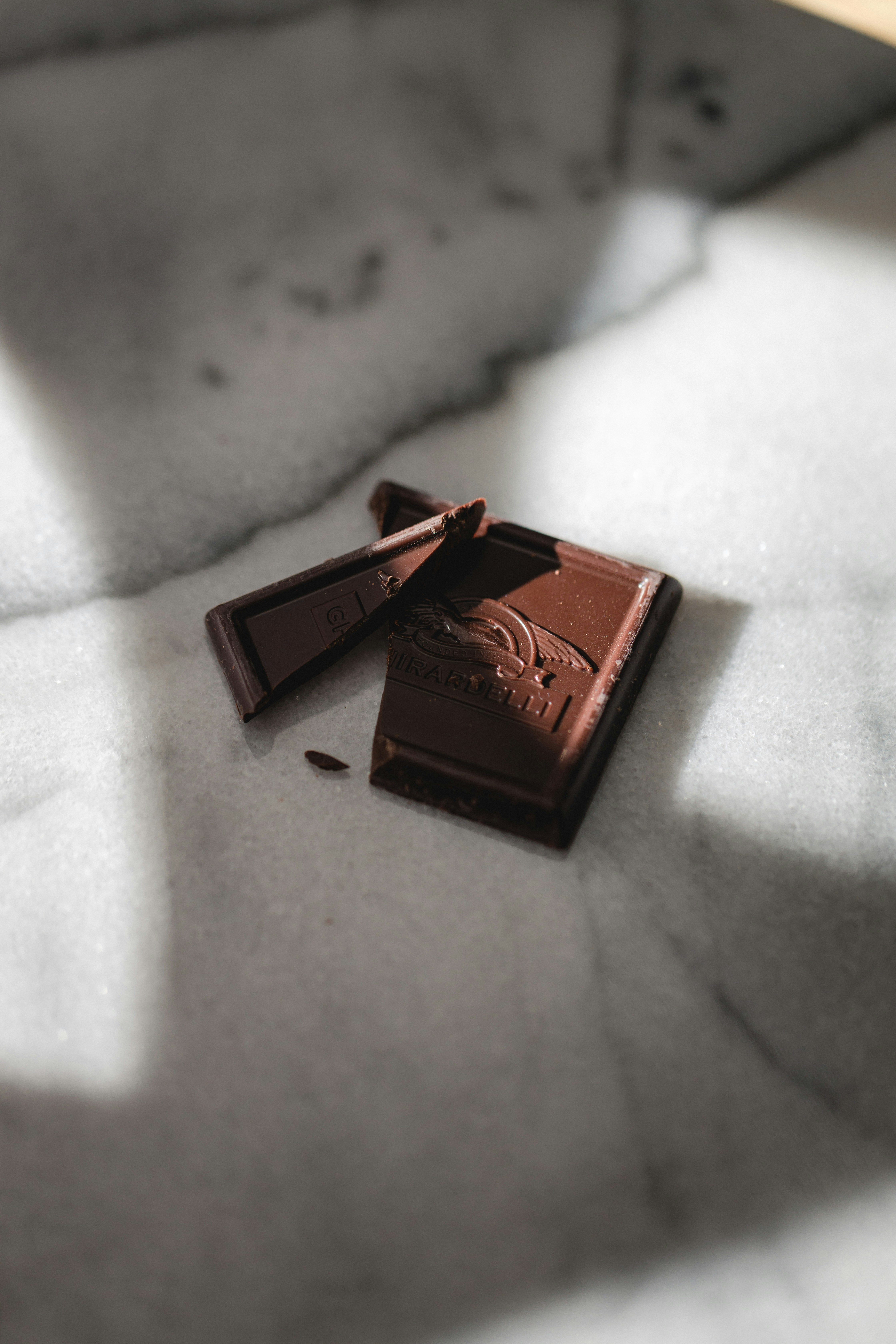 Broken square of chocolate with a decorative imprint on a marble surface.