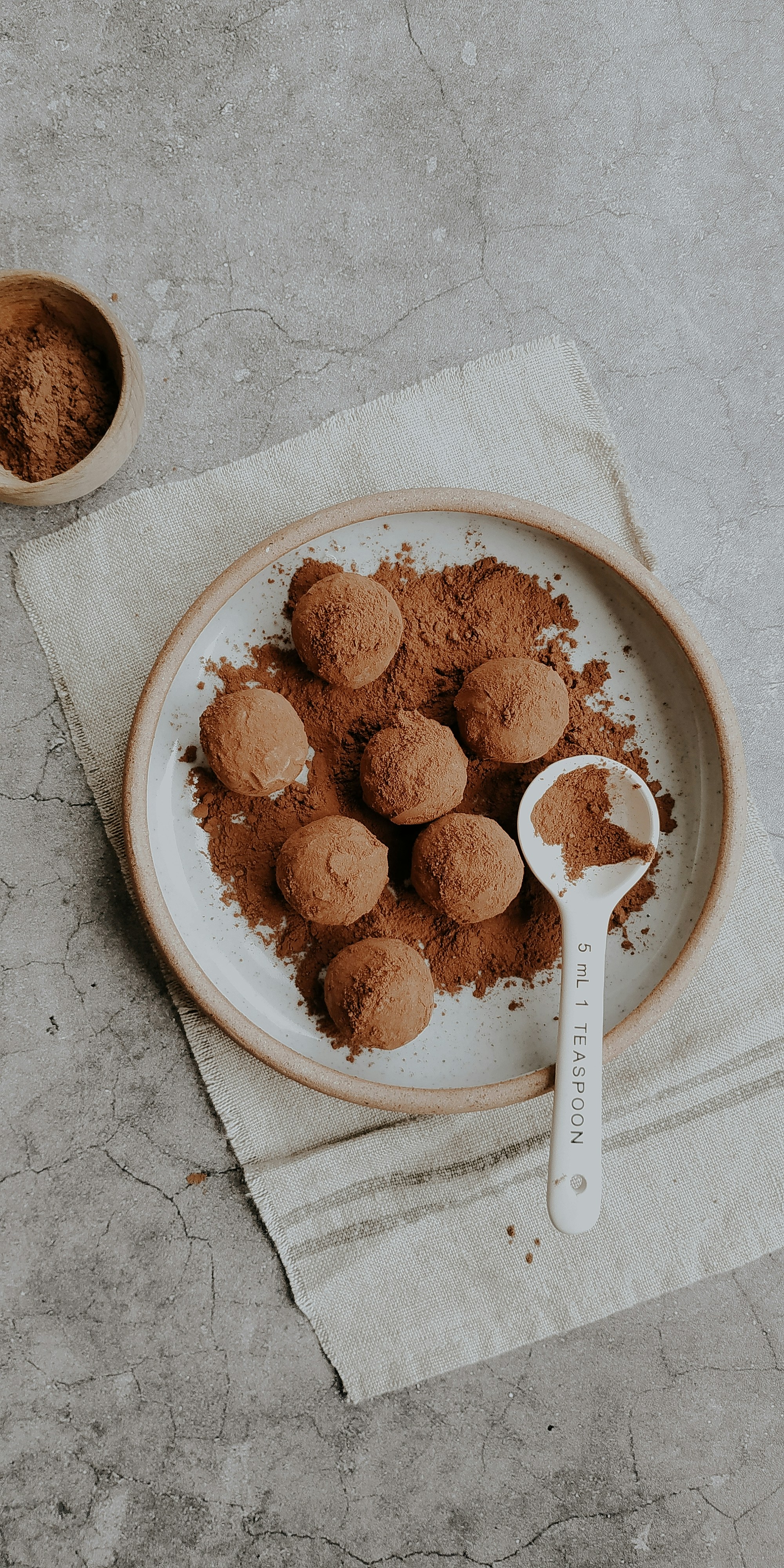 Plate of cocoa-dusted chocolate truffles with a teaspoon on a stone surface.
