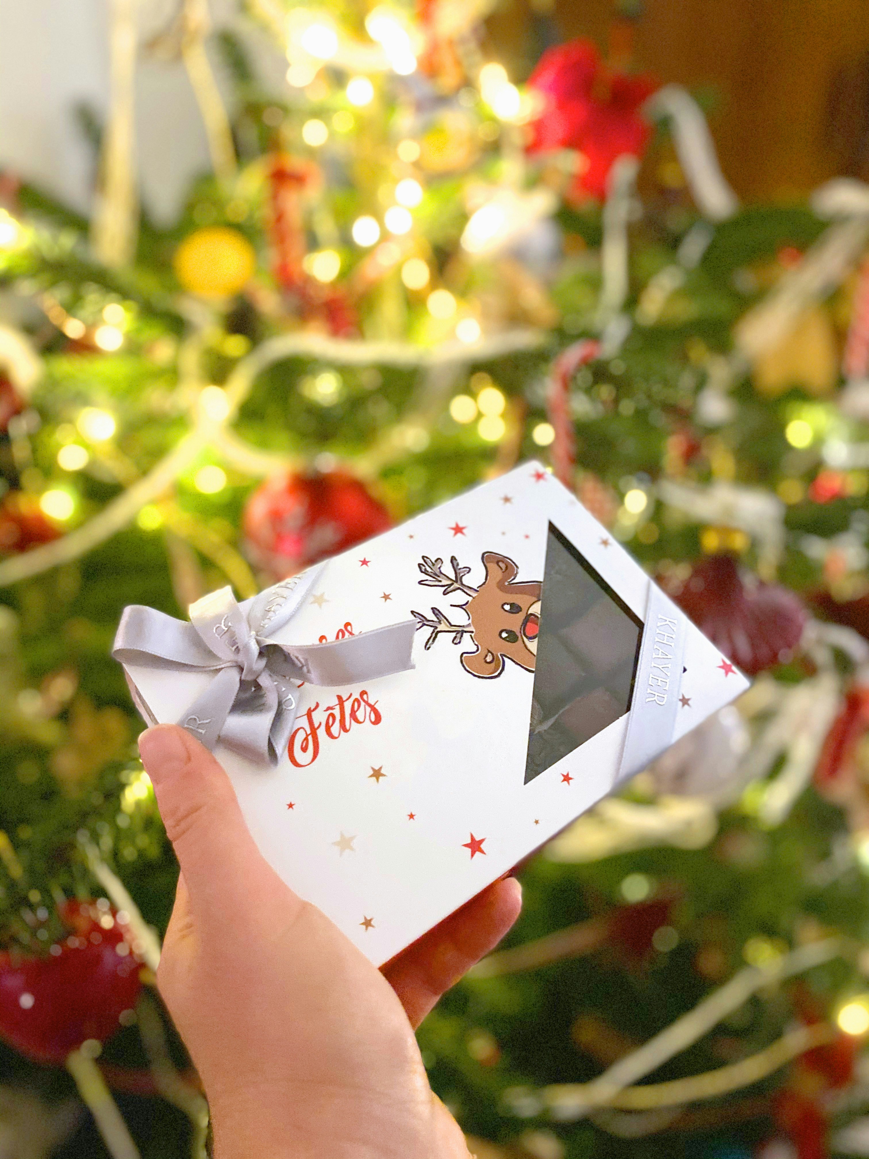 A hand holding a festive box of Christmas chocolates with a reindeer design and ribbon.