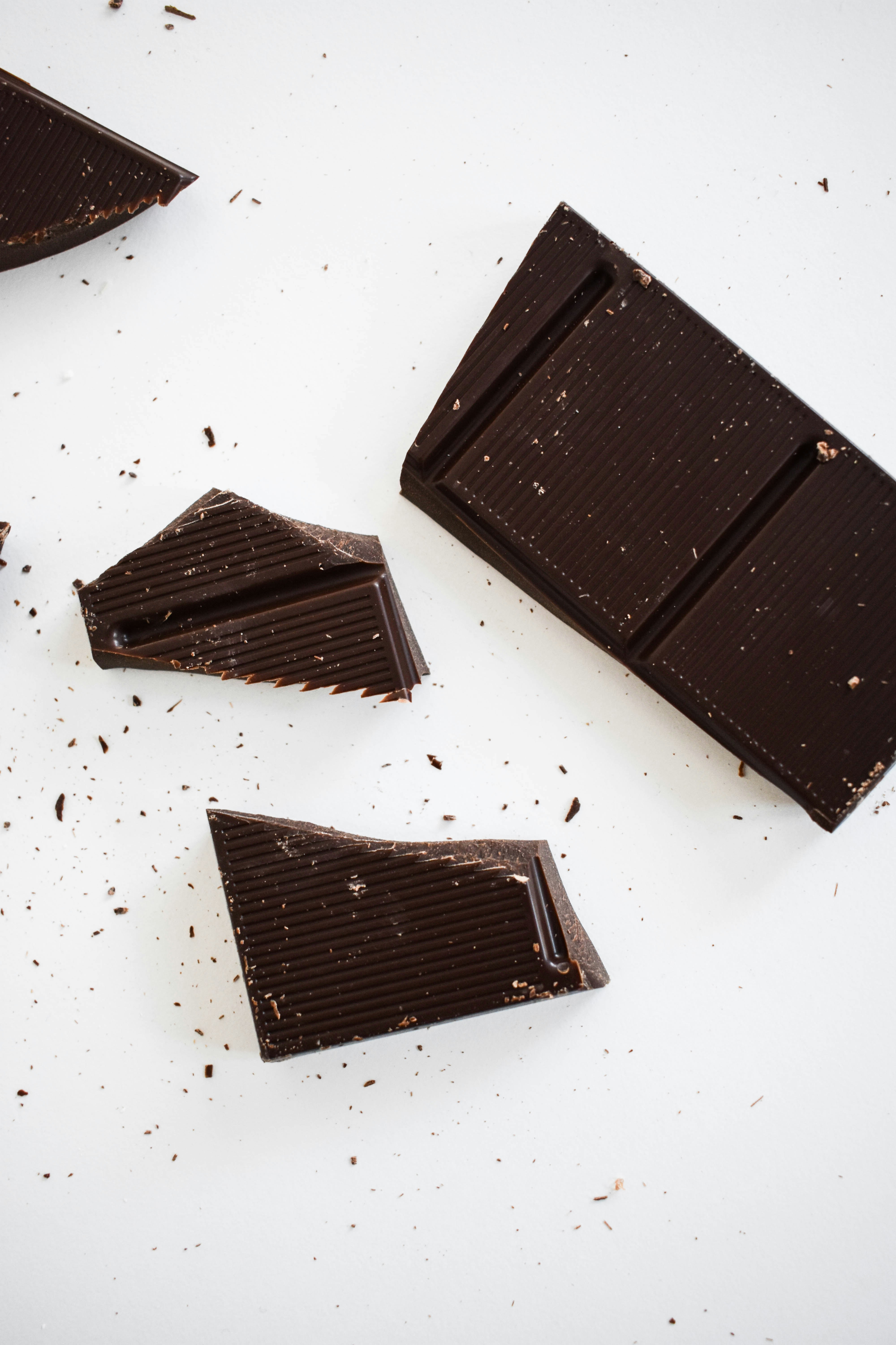 Pieces of dark chocolate on a white surface surrounded by scattered shavings.