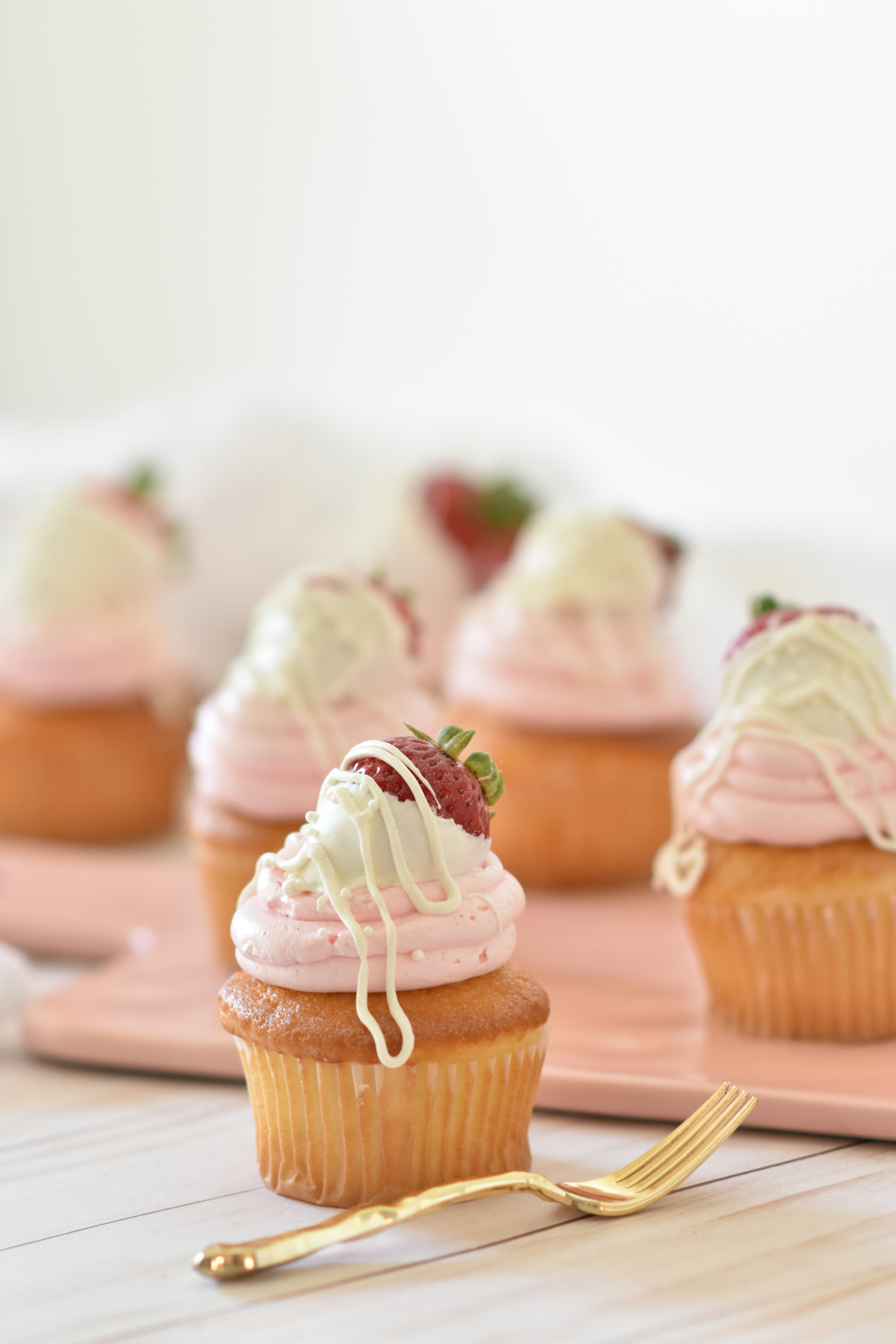 Cupcakes topped with pink and white icing and a strawberry on a light surface.