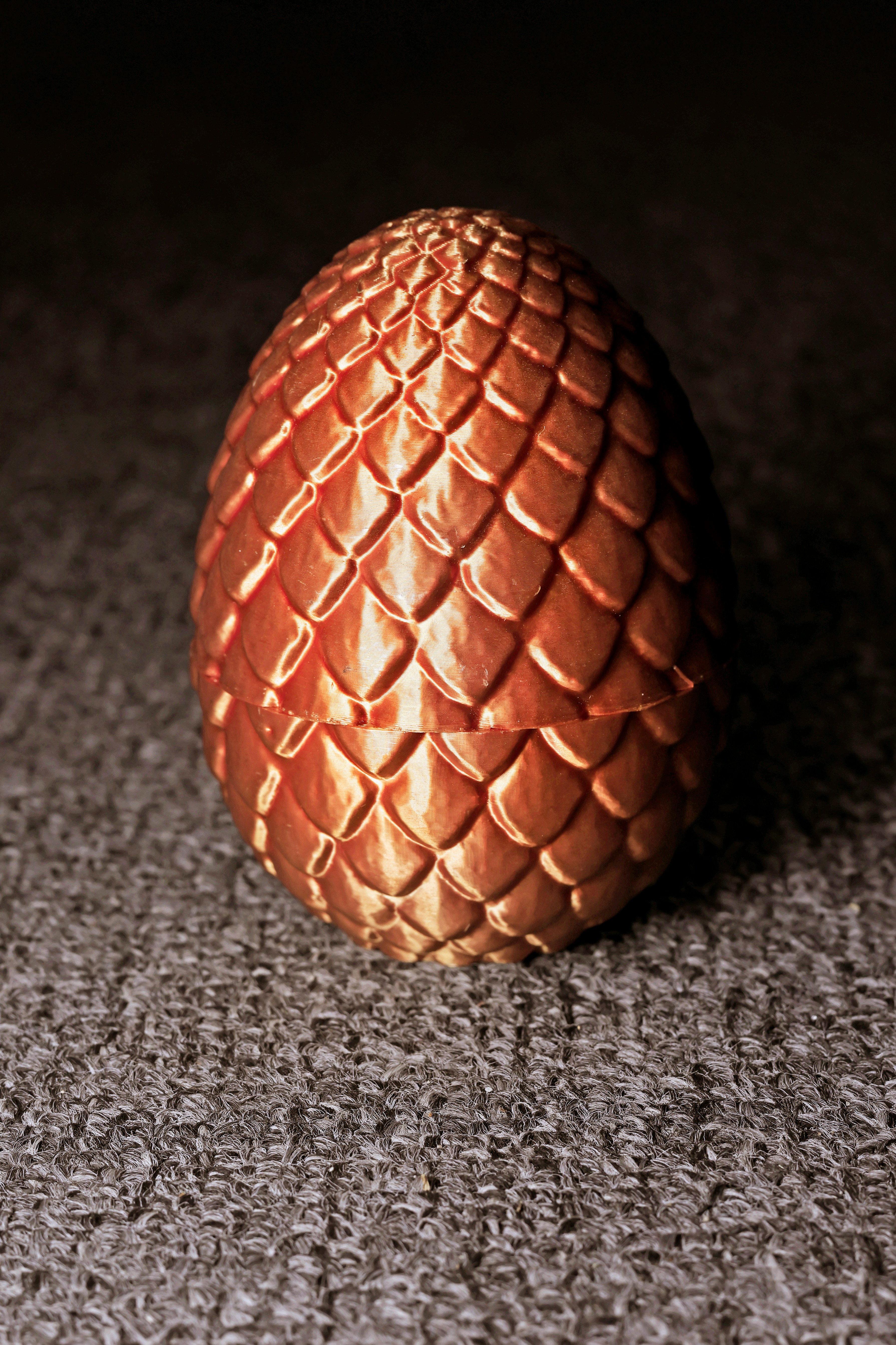 A glossy milk chocolate Easter egg with a patterned shell on a dark surface.