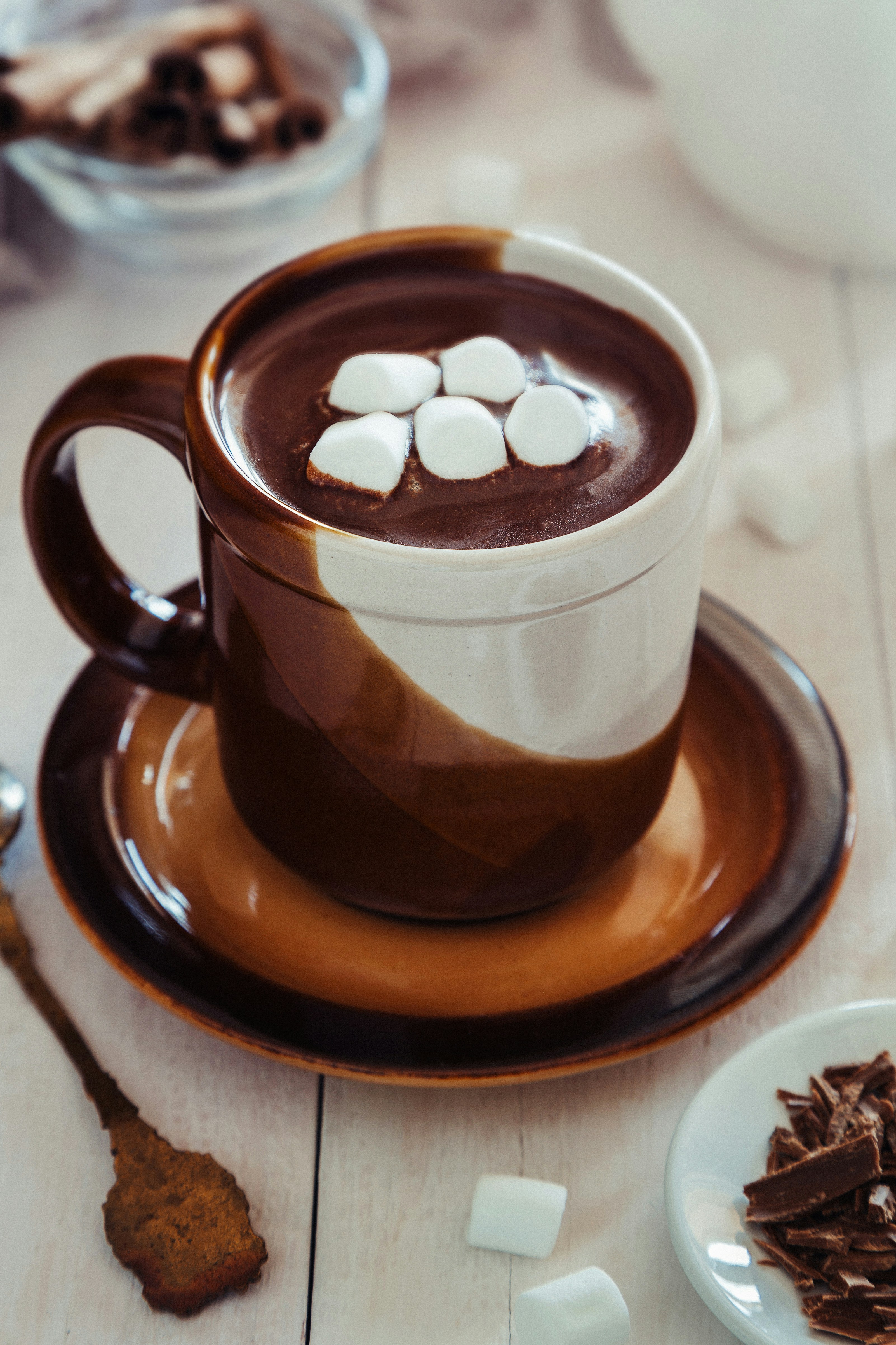 Mug of hot chocolate topped with white marshmallows placed on a light wooden table.