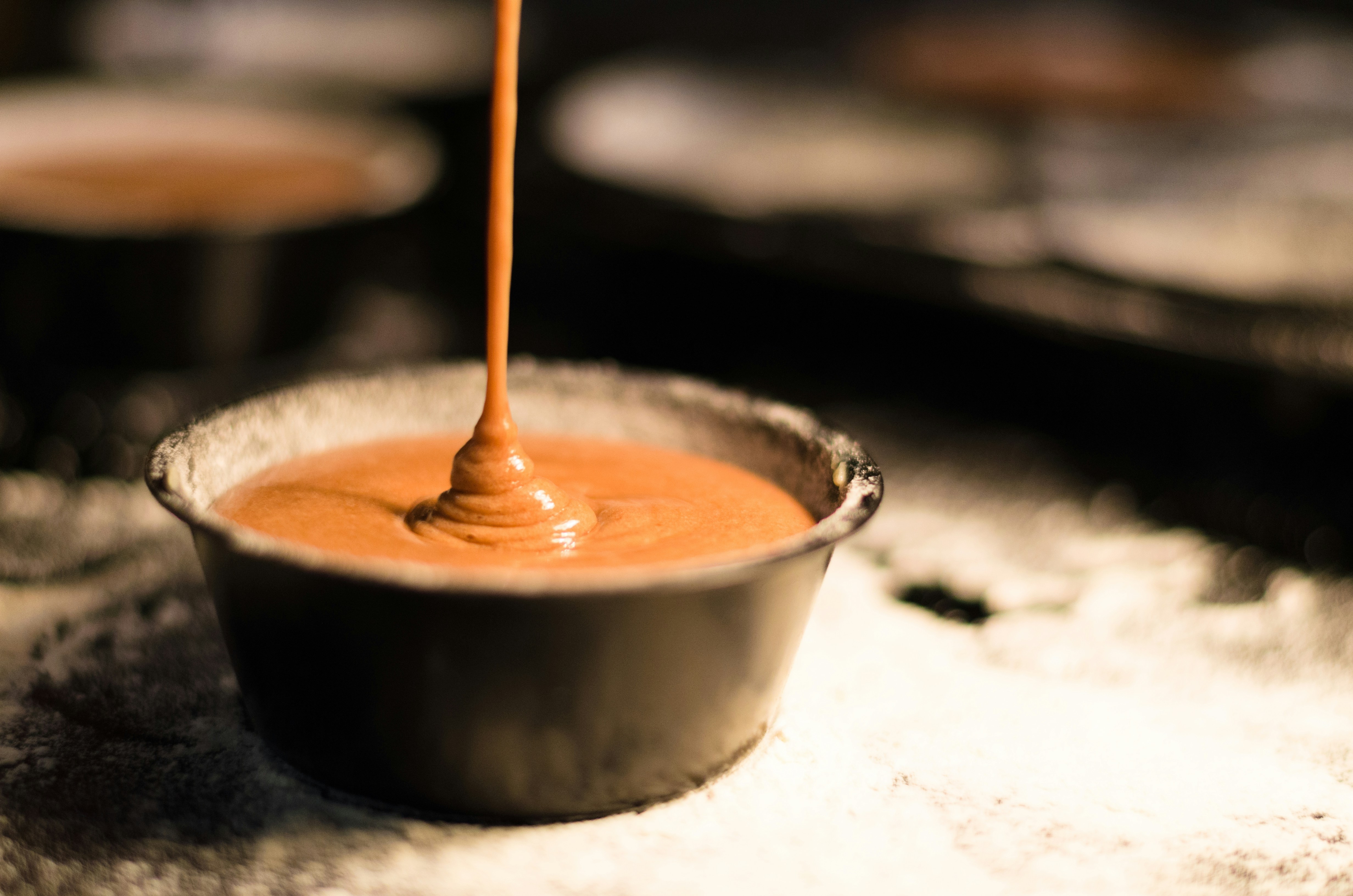 Peanut butter being poured into a ceramic bowl.