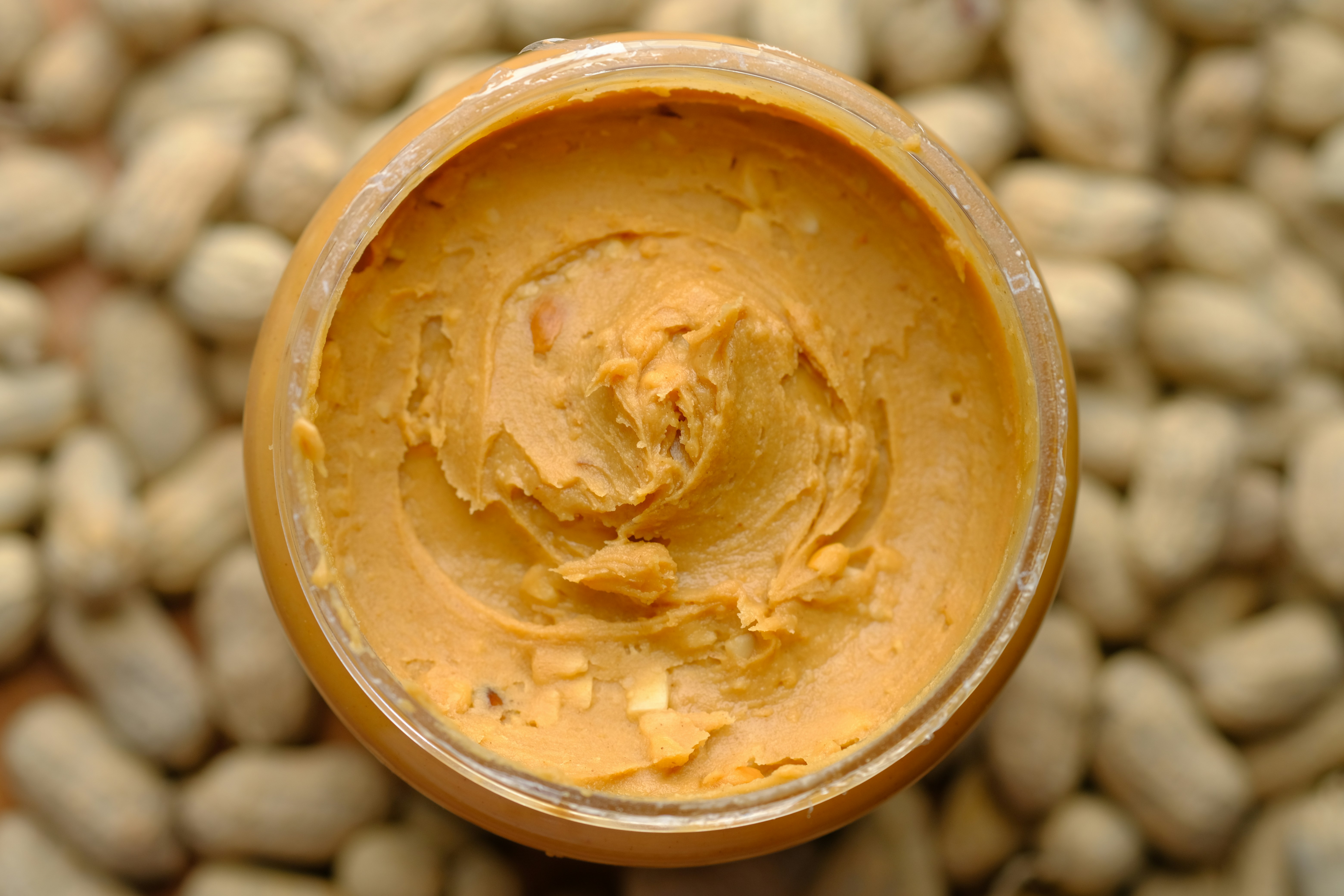 Smooth peanut butter with peanuts in background.